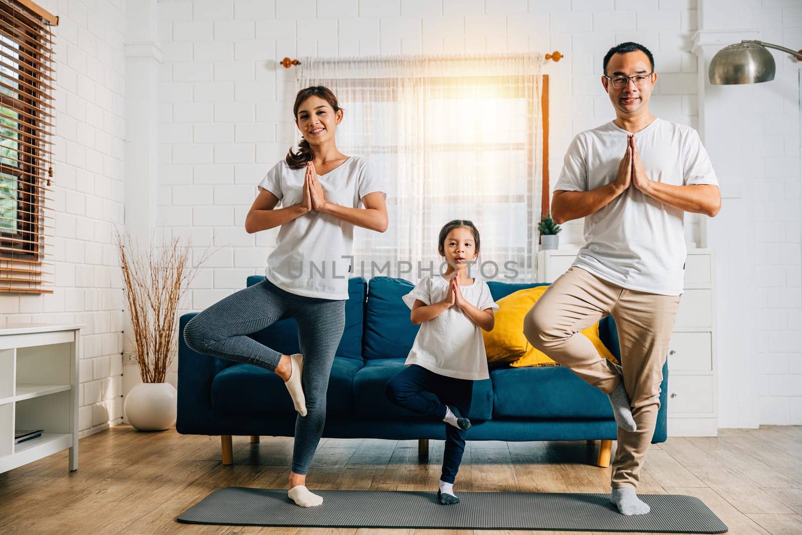 Asian parents and their daughter bond through yoga and fitness training on the living room floor emphasizing health happiness and togetherness during their family weekend.
