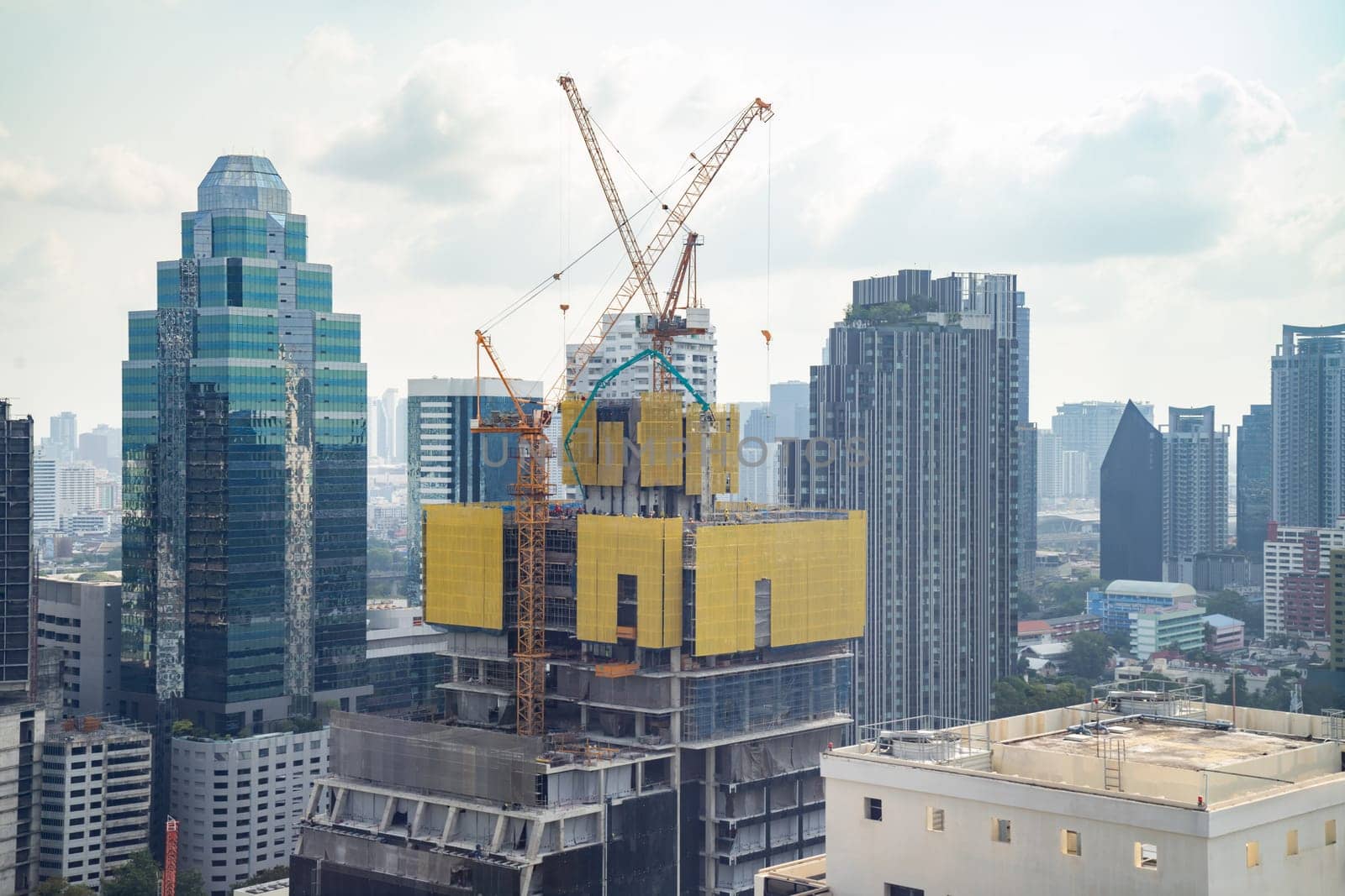 Image of exterior skyscrapers construction site with tower cranes. Cityscape under construction with cranes working moving to renovate building. Blue sky background. Architectural. Ornamented.