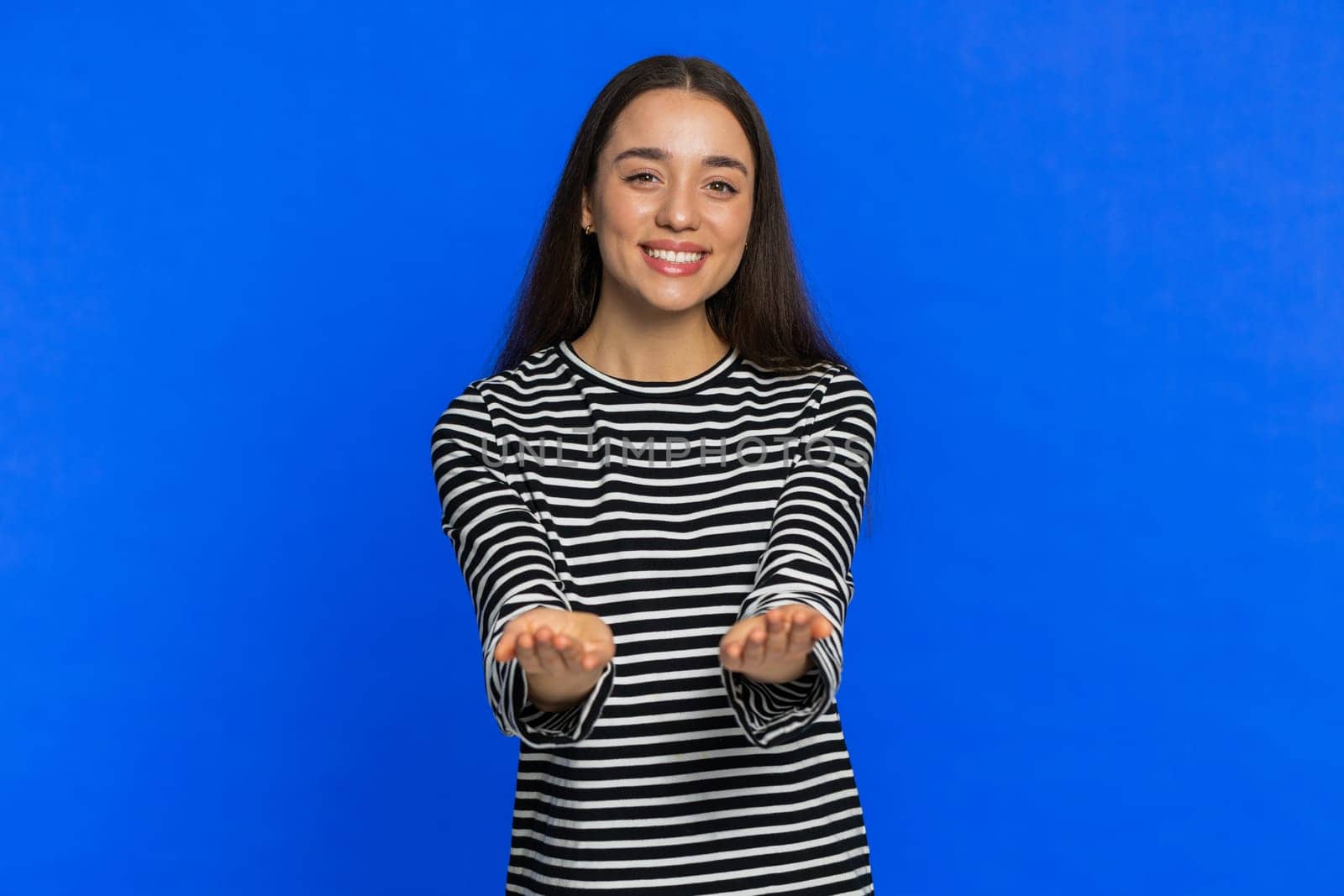 Free gifts and presents for you. Caucasian young woman in striped blouse opening hands, excitement, preparing surprise, sharing love emotions, congratulating, charity donation. Girl on blue background