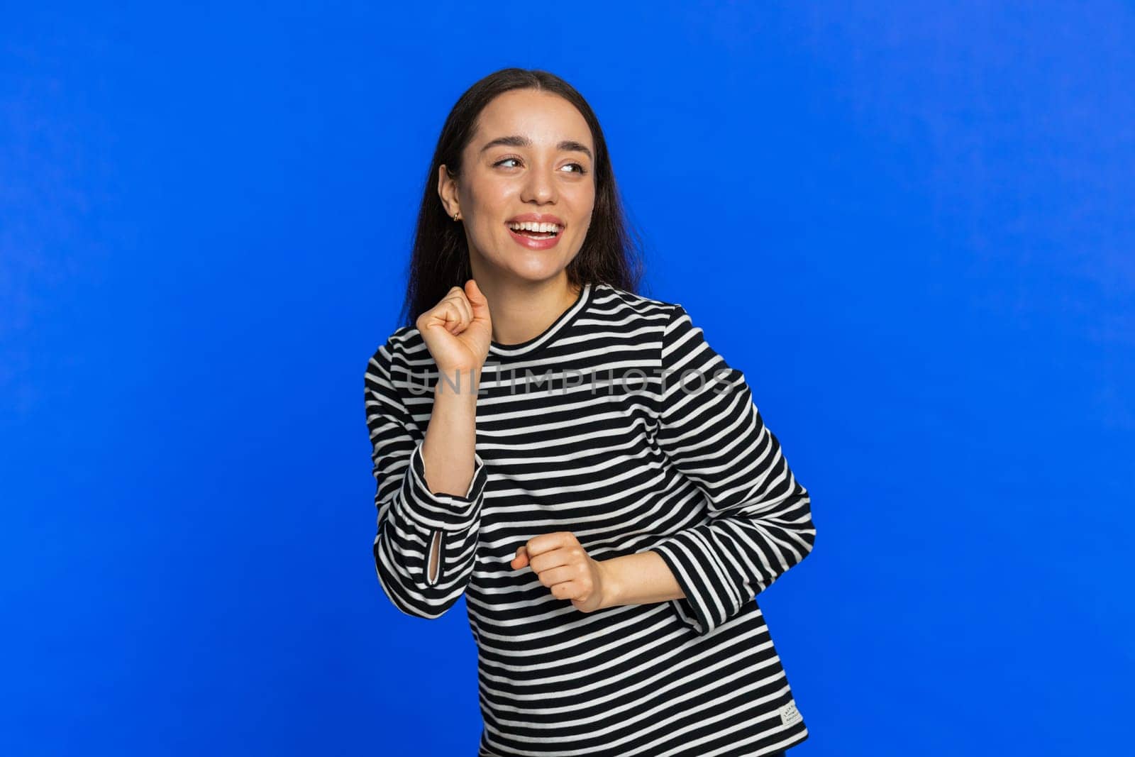 Stylish Caucasian woman listening music dancing disco fooling around having fun celebrating success victory winning play game good positive news achievement. Happy girl isolated on blue background