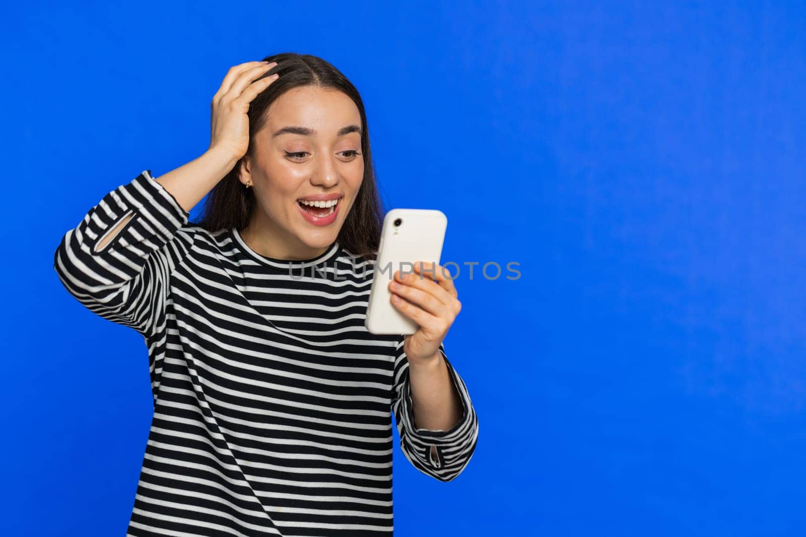 Happy excited young woman girl use smartphone typing browsing shouting say wow yes found out great big win good news lottery goal achievement celebrating success, winning play game on blue. Copy-space