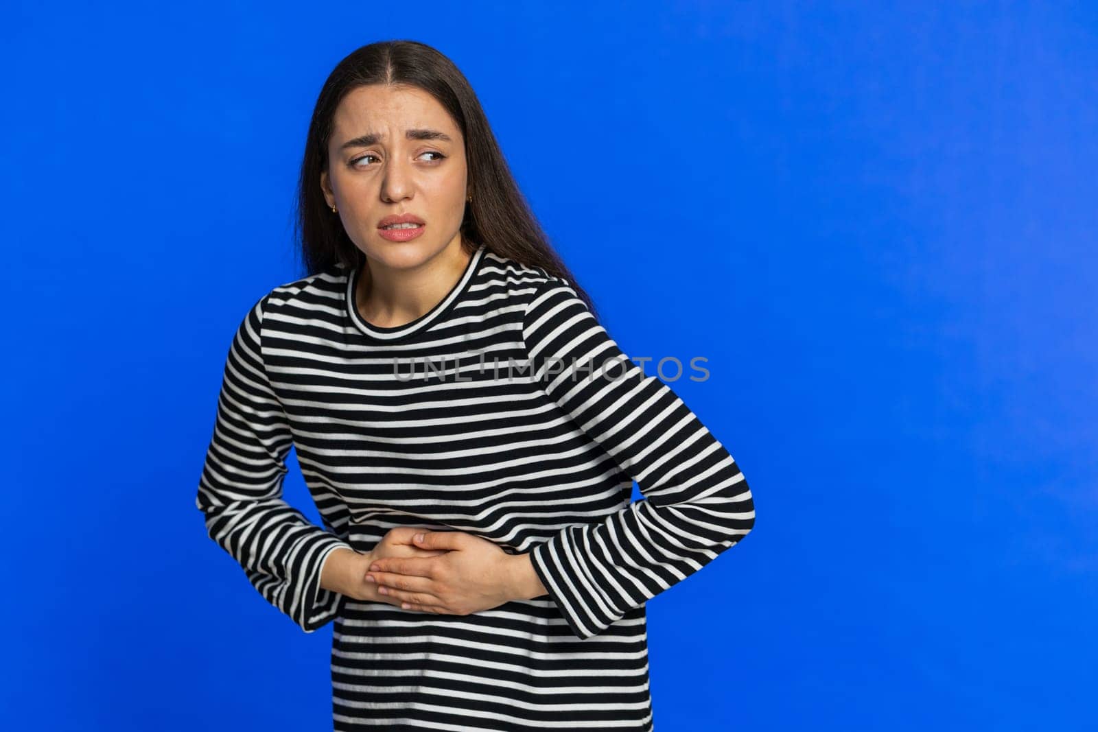 Sick ill woman in striped blouse suffering from period cramps, painful stomach ache. Girl holding belly feeling abdominal or menstrual pain. Abdominal pain gastritis diarrhea indigestion. Copy-space