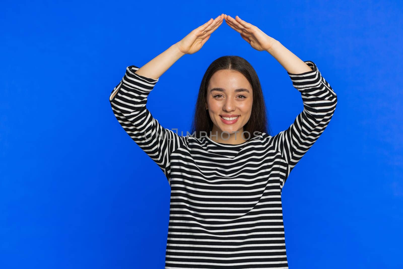 House roof about head. Young woman playing childish catching up game feeling in safe making roof above head with hands, insurance, security service. Girl isolated on blue studio background. Copy-space