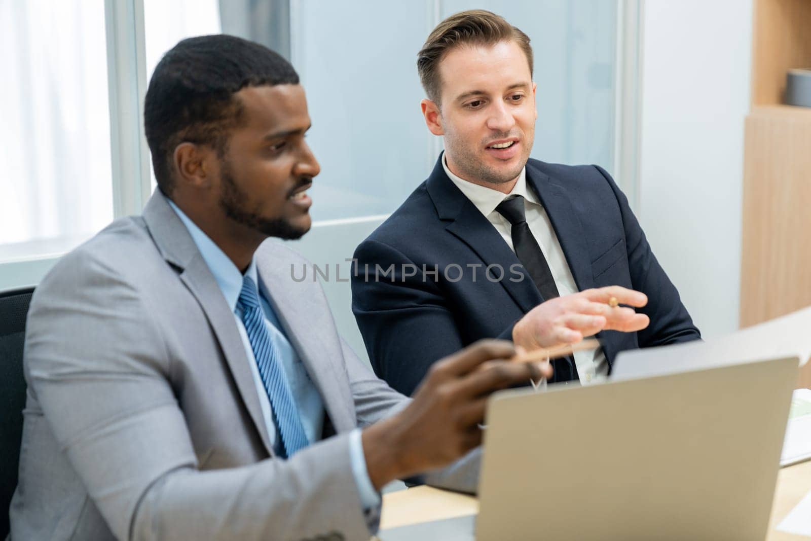 African male leader explain strategy while show solution to professional project manager by pointing at document, using laptop. Skilled business team brainstorming idea. Business meeting. Ornamented.