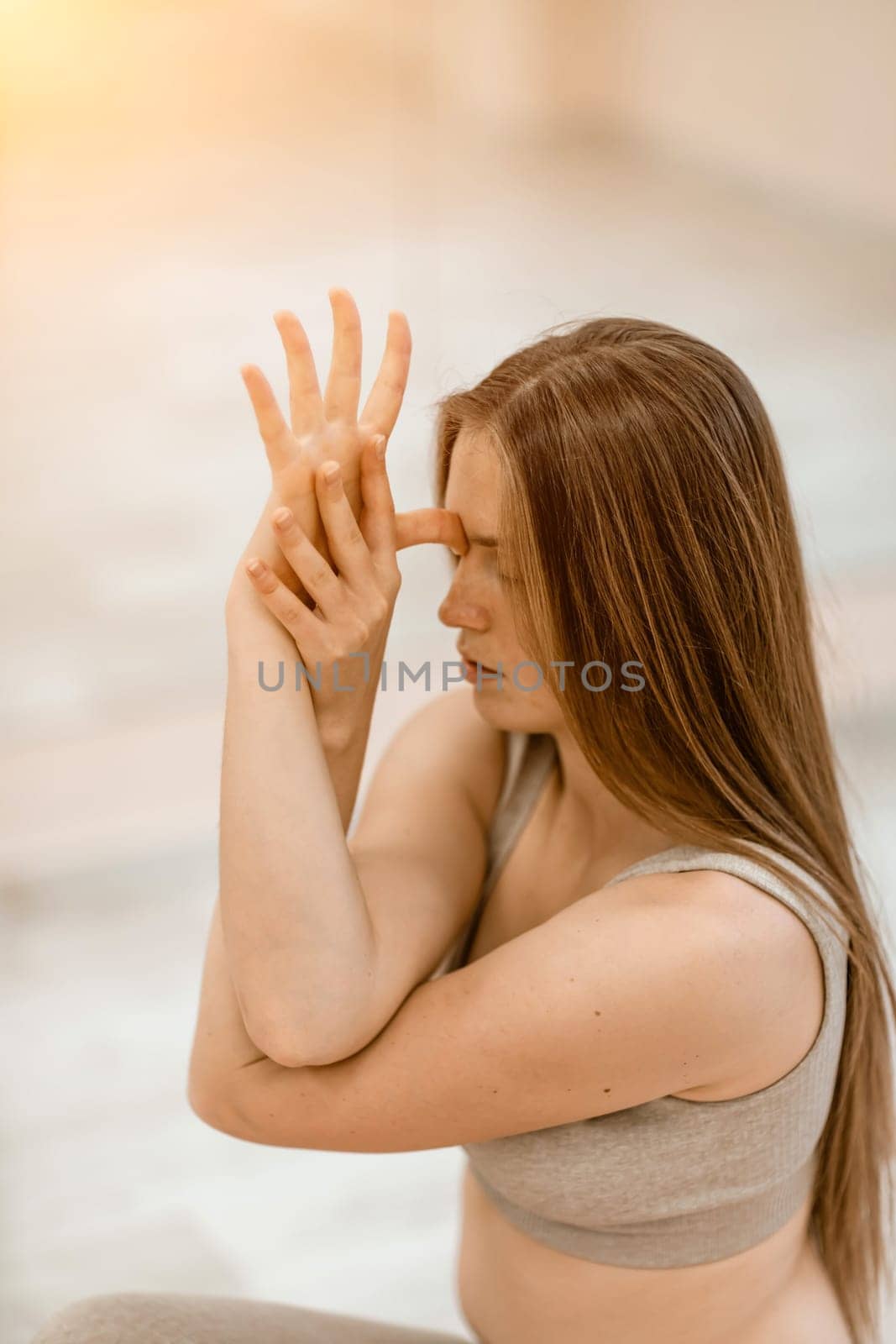 Young woman doing yoga in the gym. A girl with long hair and in a beige tracksuit stands in a cow pose on a pink carpet. A woman performs Gomukhasana. by Matiunina