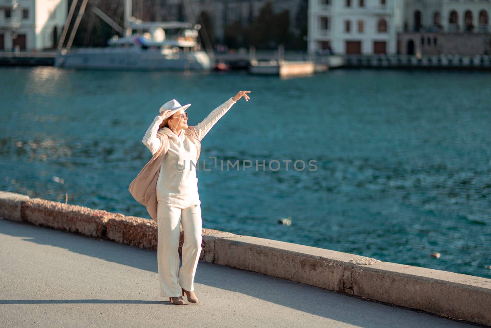 Happy blonde woman in a white suit and hat posing at the camera against the backdrop of the sea by Matiunina