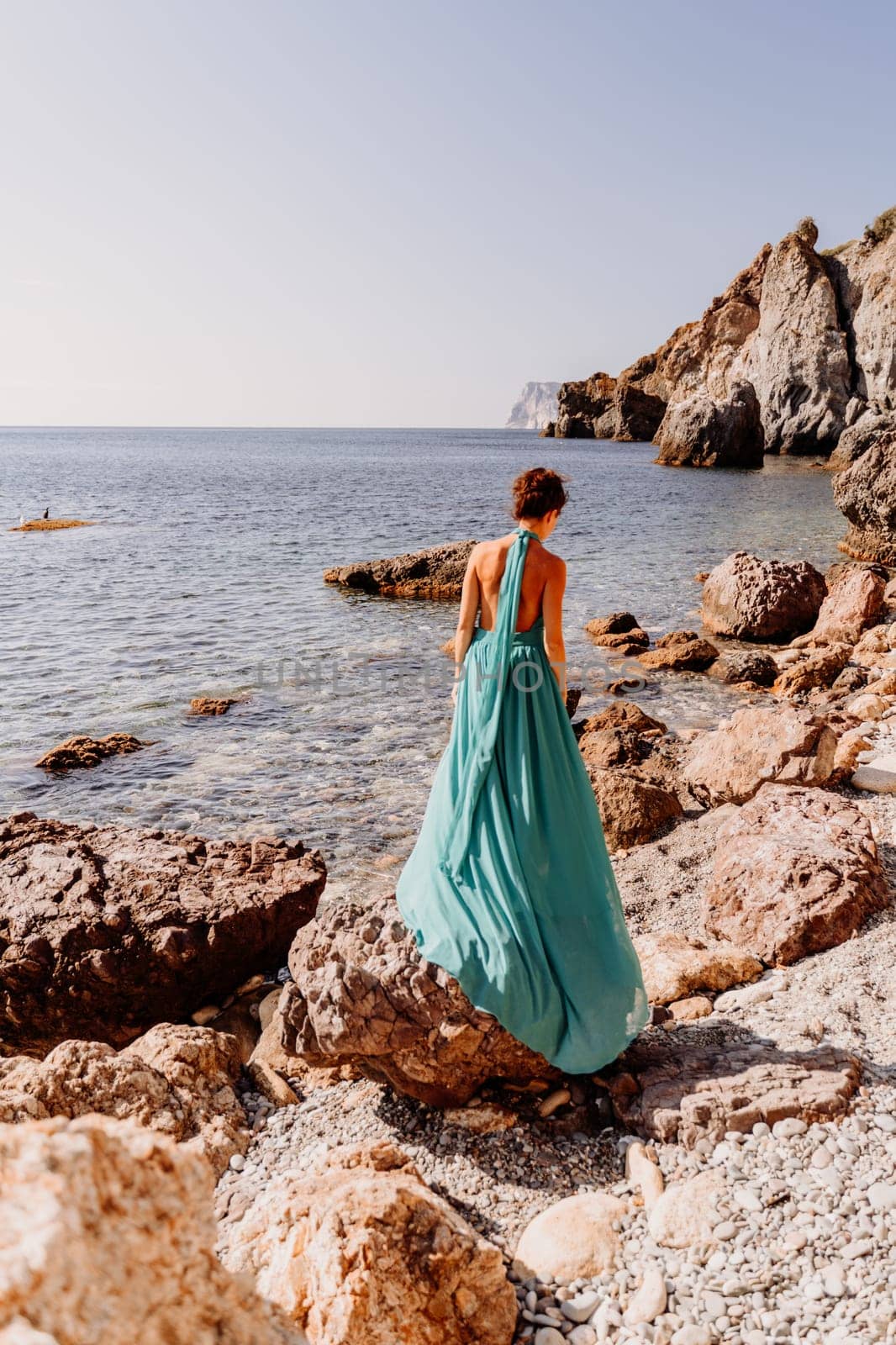 Woman green dress sea. Woman in a long mint dress posing on a beach with rocks on sunny day. Girl on the nature on blue sky background. by Matiunina