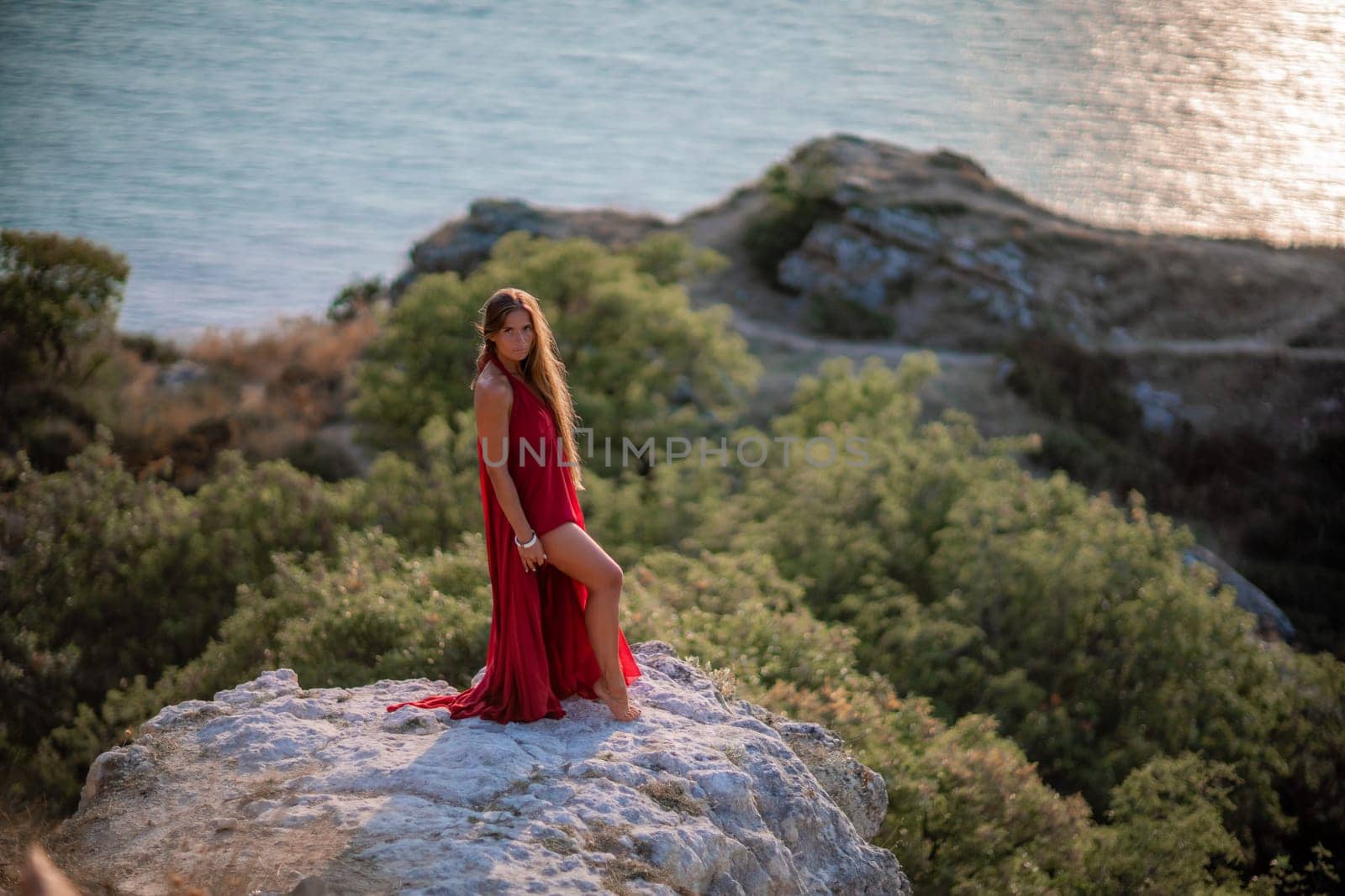 Woman sunset sea red dress, back view a happy beautiful sensual woman in a red long dress posing on a rock high above the sea on sunset. by Matiunina