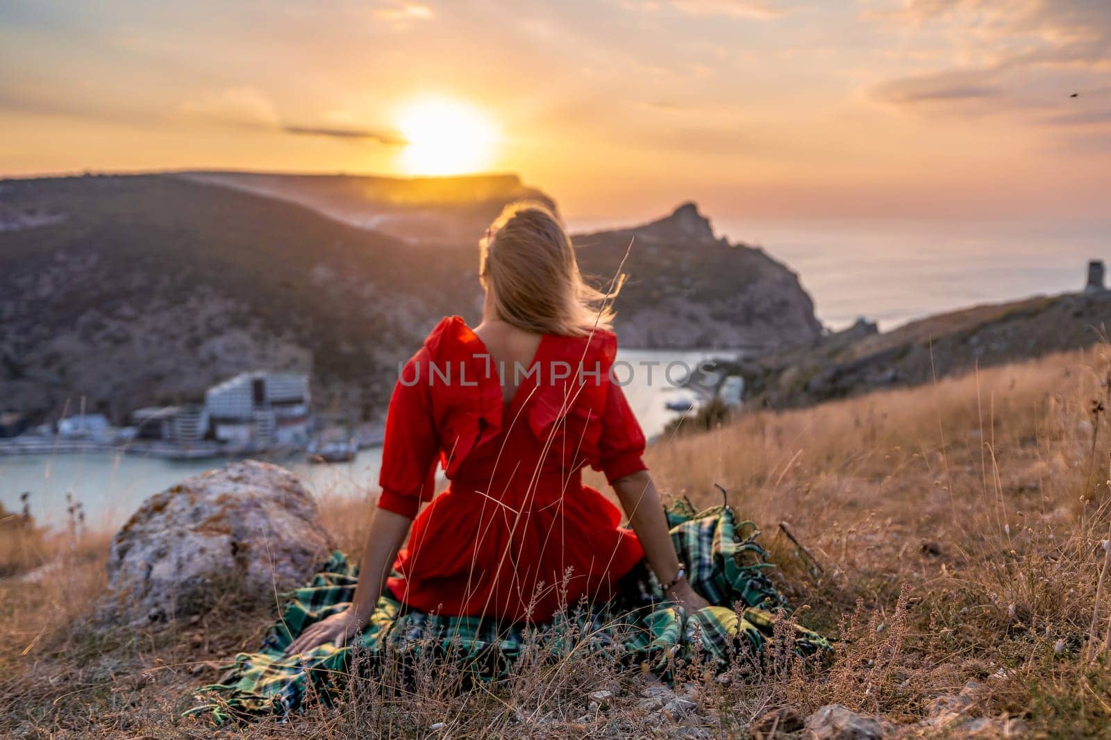 Woman sunset sea mountains. Happy woman siting with her back on the sunset in nature summer posing with mountains on sunset, silhouette. Woman in the mountains red dress, eco friendly, summer landscape active rest.