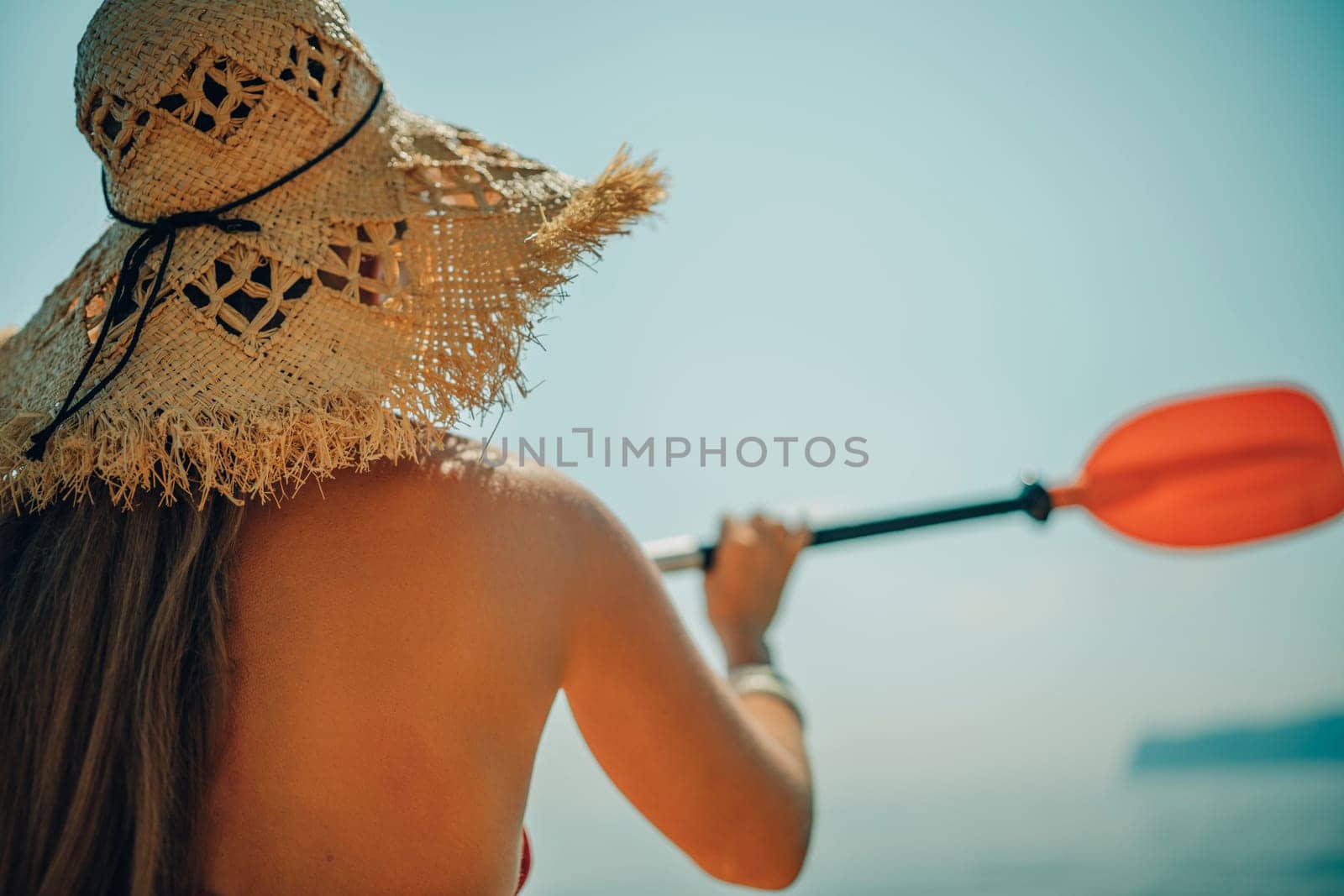 Woman in kayak back view. Happy woman with long hair in a swimsuit and hat floating in kayak on the sea. Summer holiday vacation. Summer holidays vacation at sea