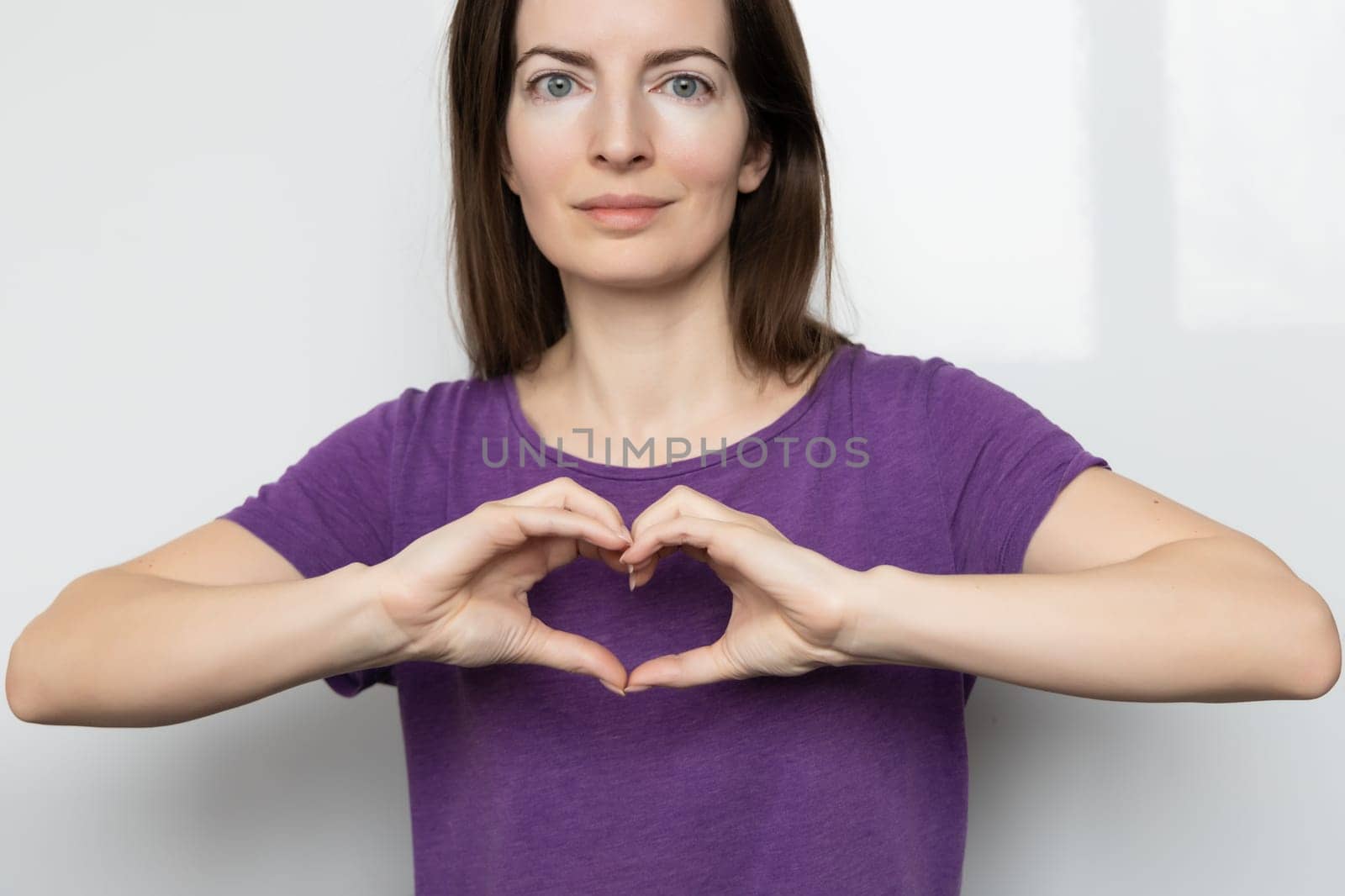 Inspire inclusion. Woman holding her hands in the shape of a heart and holding them in front of her, dressed purple t-shirt. International women's day concept