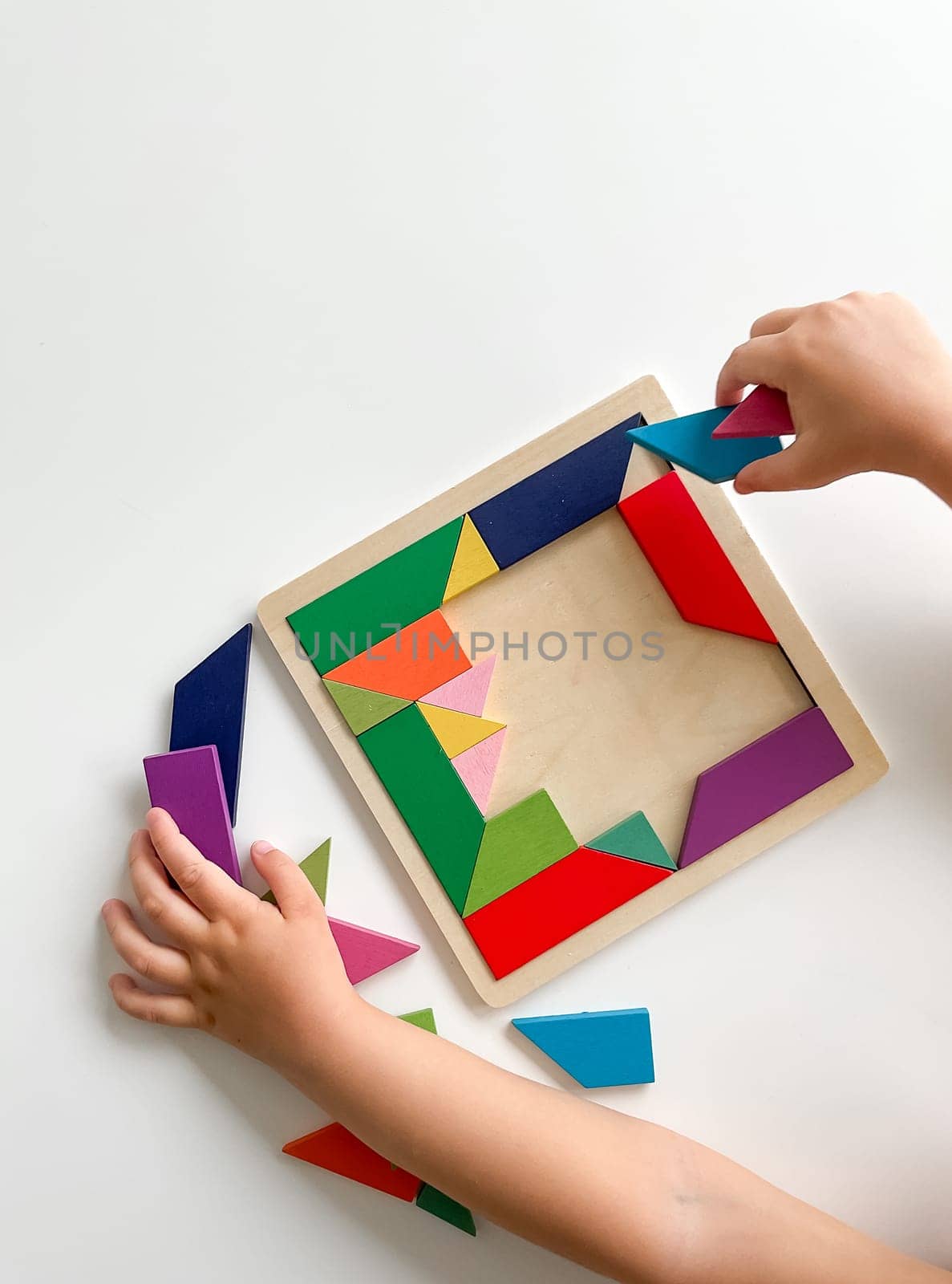 childs hand collects multicolored wooden mosaic on white background. by Lunnica