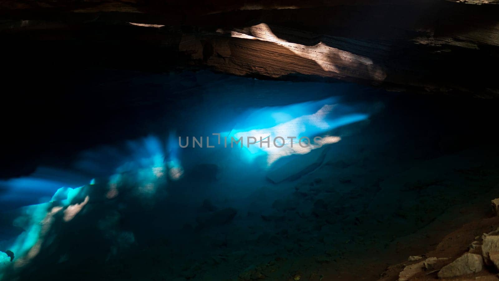 Sunlight pierces a cave, lighting up its blue waters.