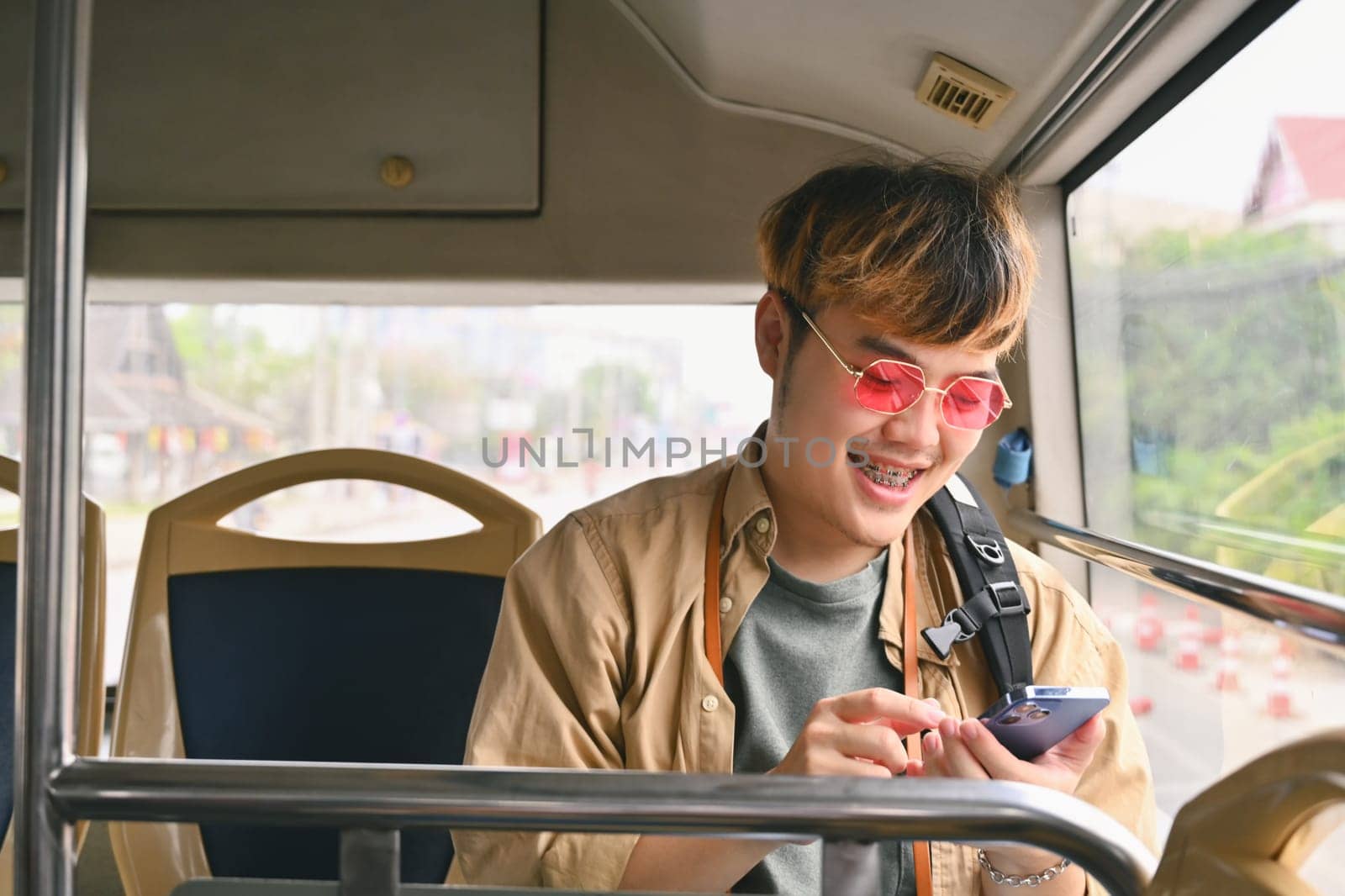 Happy smiling man sitting on a bus seat as a travel passenger and using mobile phone.