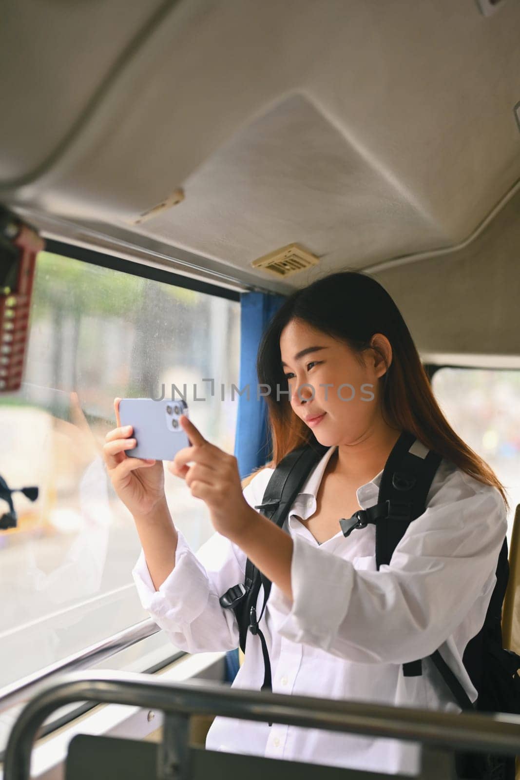 Smiling young woman taking photos trough the window with smartphone.Travel and transportation concept by prathanchorruangsak