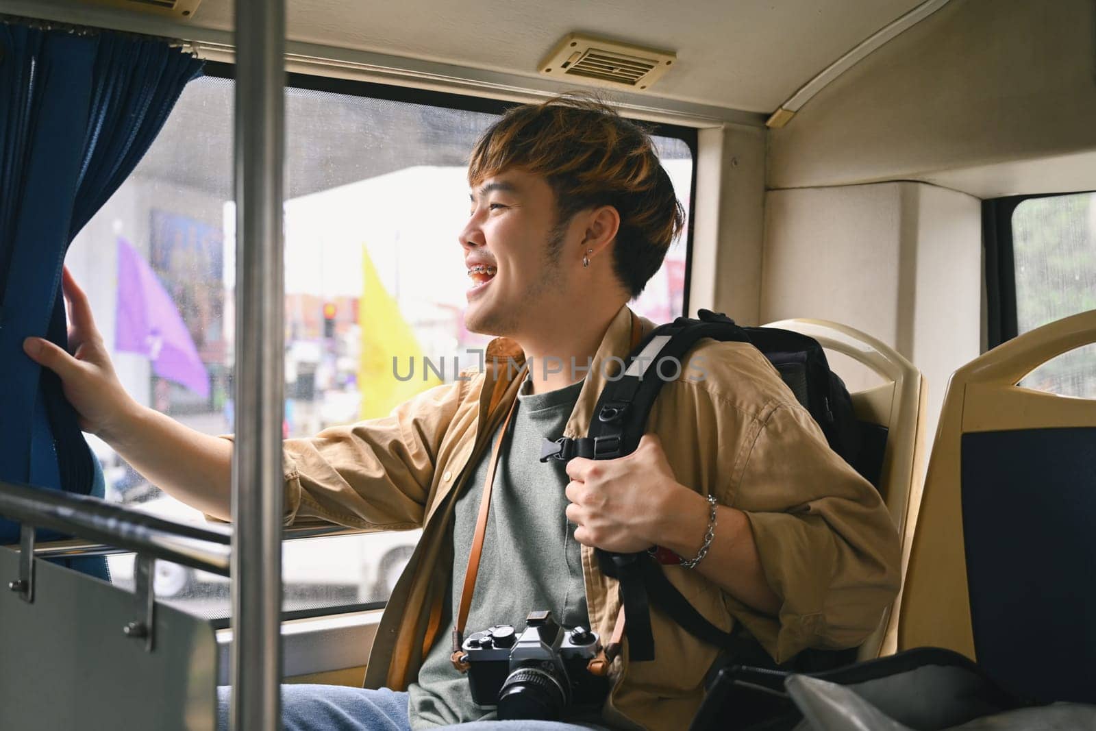 Cheerful Asian man sitting and looking through the bus window. Travel and transportation concept.