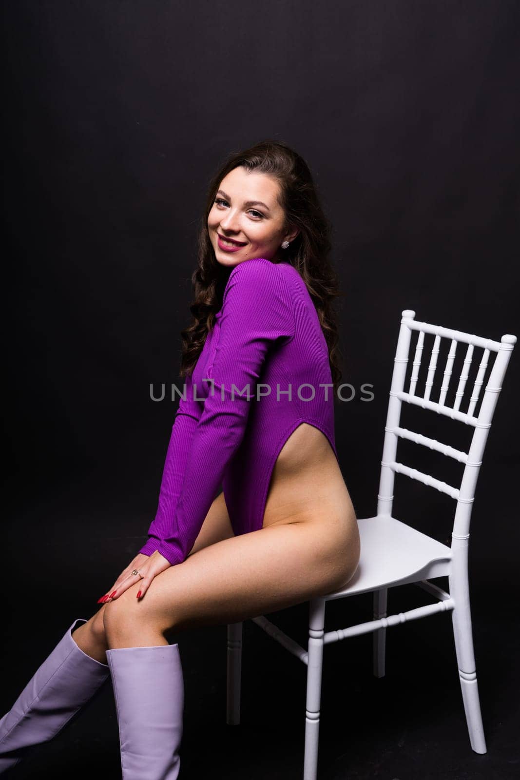 Slender seductive brunette female in a violet bodysuit against a dark background. by Zelenin