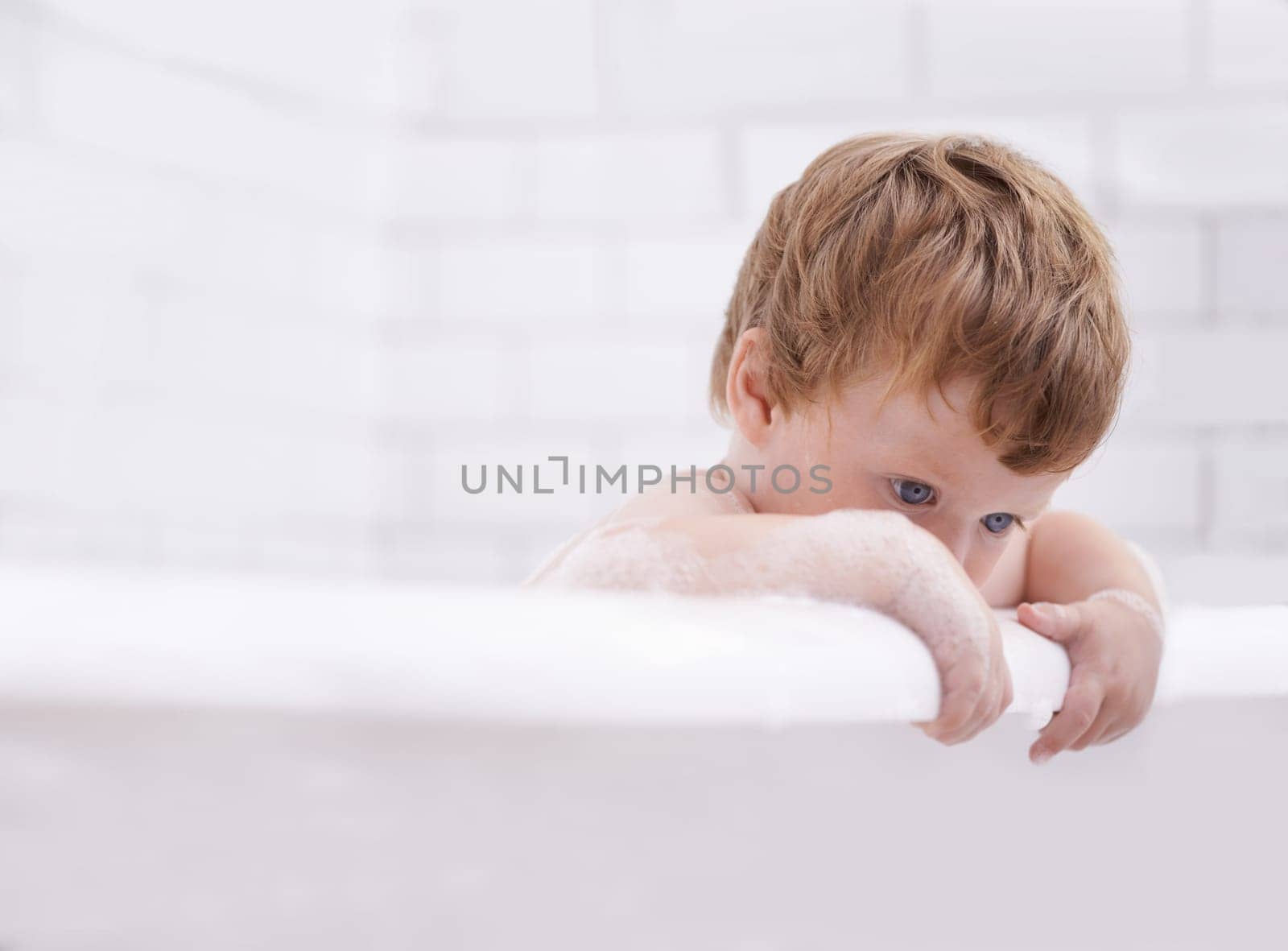 Baby, bath and washing with bubbles and thinking in the bathroom at home for hygiene. Grooming, brunette and boy child cleaning for bodycare in the house while curious for development and growth by YuriArcurs