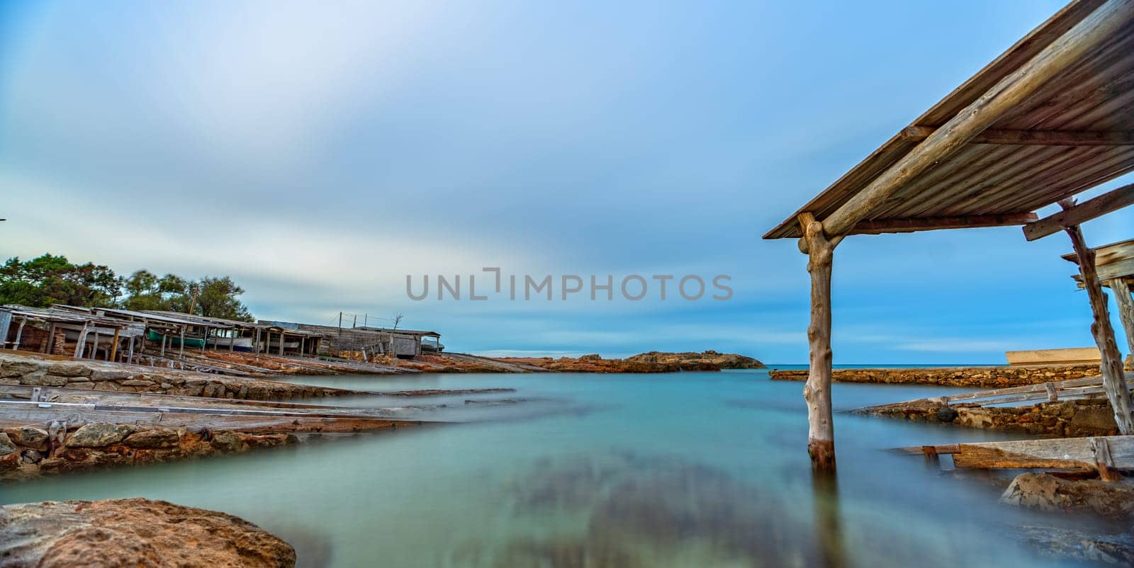 Long exposure shot of a historic dock with rails for launching fishing boats into a clear sea under cloudy skies.