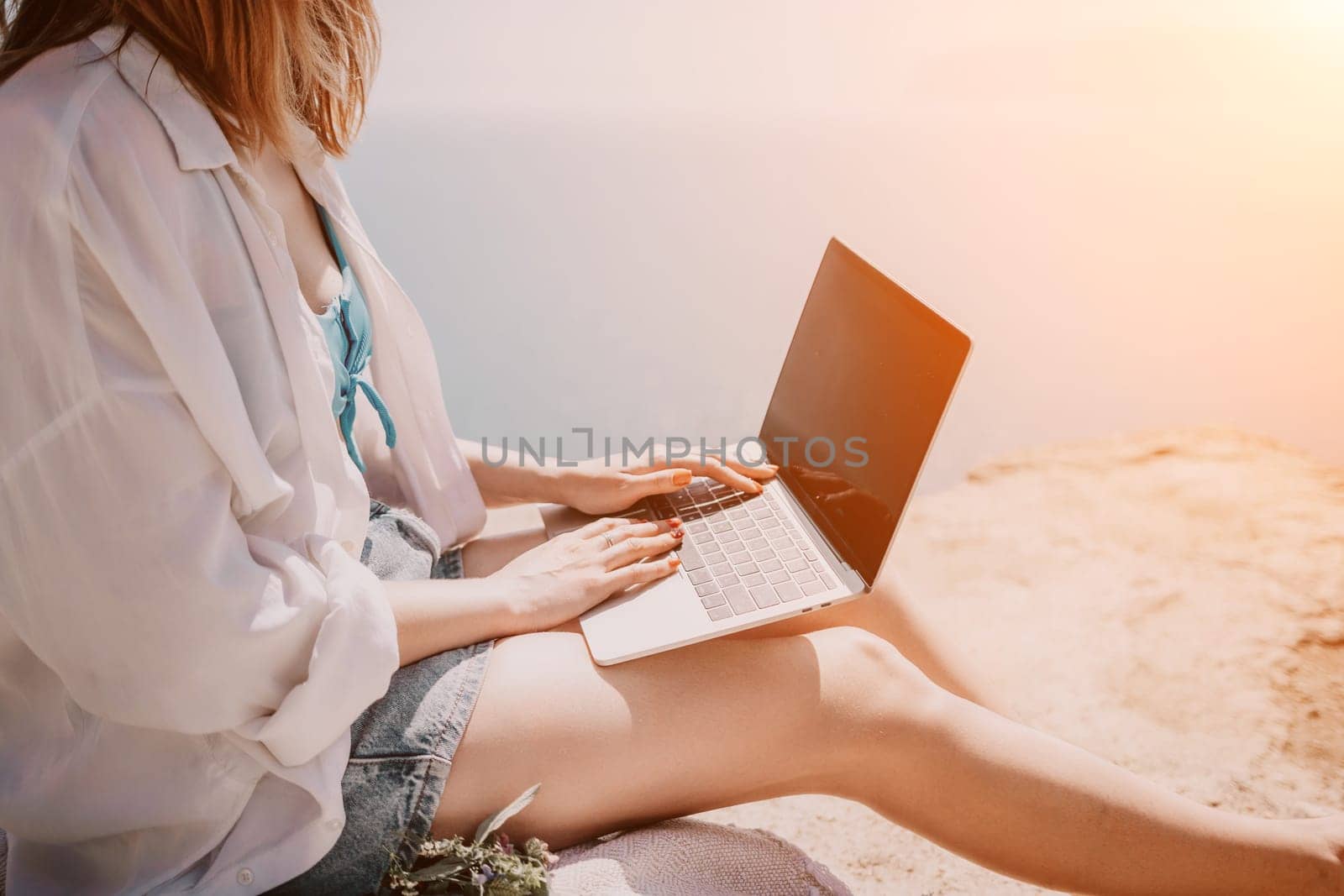 Woman sea laptop. Successful business woman working on laptop by the sea. Pretty lady typing on computer at summer day outdoors. Freelance, digital nomad, travel and holidays concept. by panophotograph