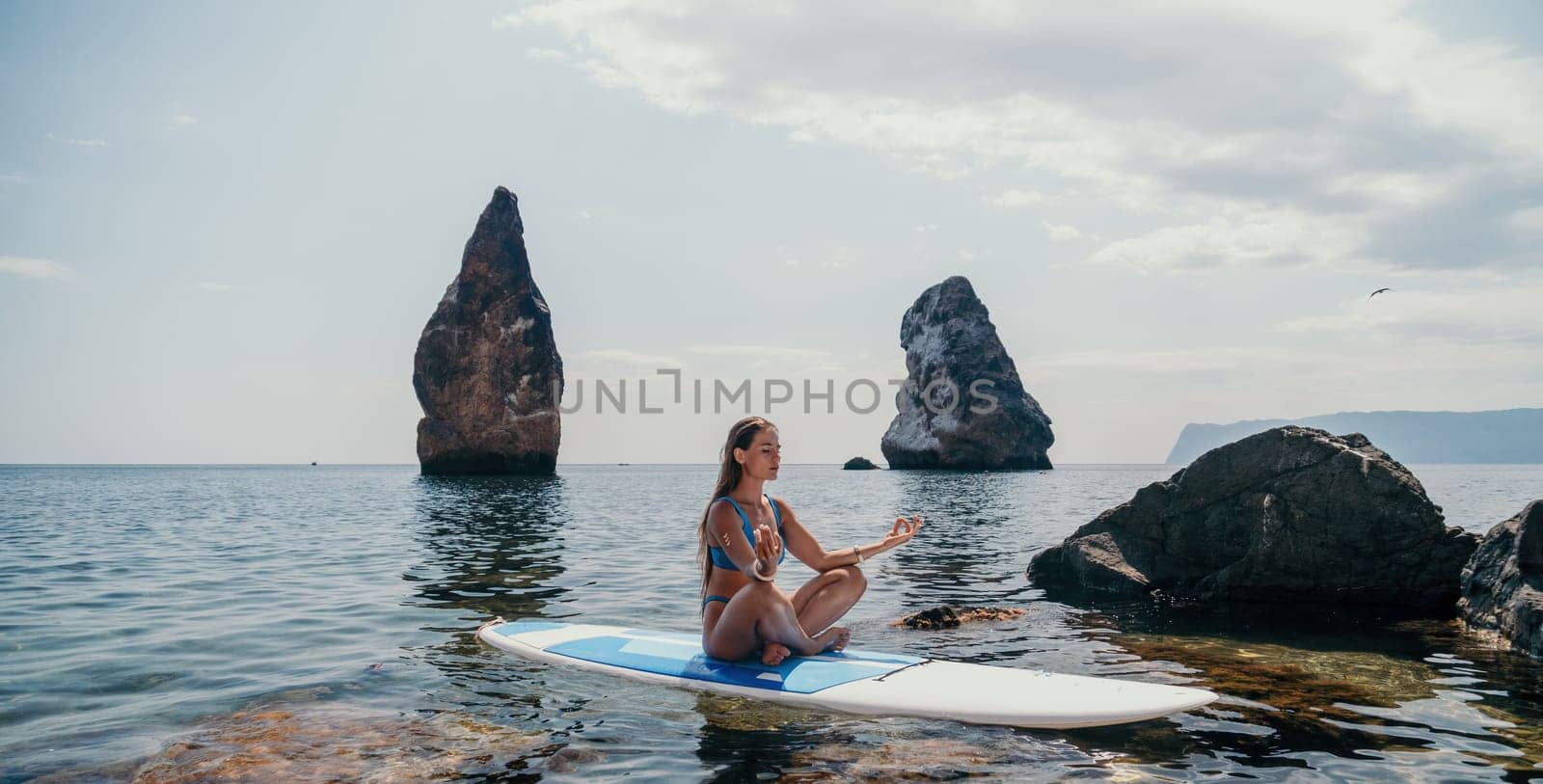 Woman sup yoga. Middle age sporty woman practising yoga pilates on paddle sup surfboard. Female stretching doing workout on sea water. Modern individual hipster outdoor summer sport activity