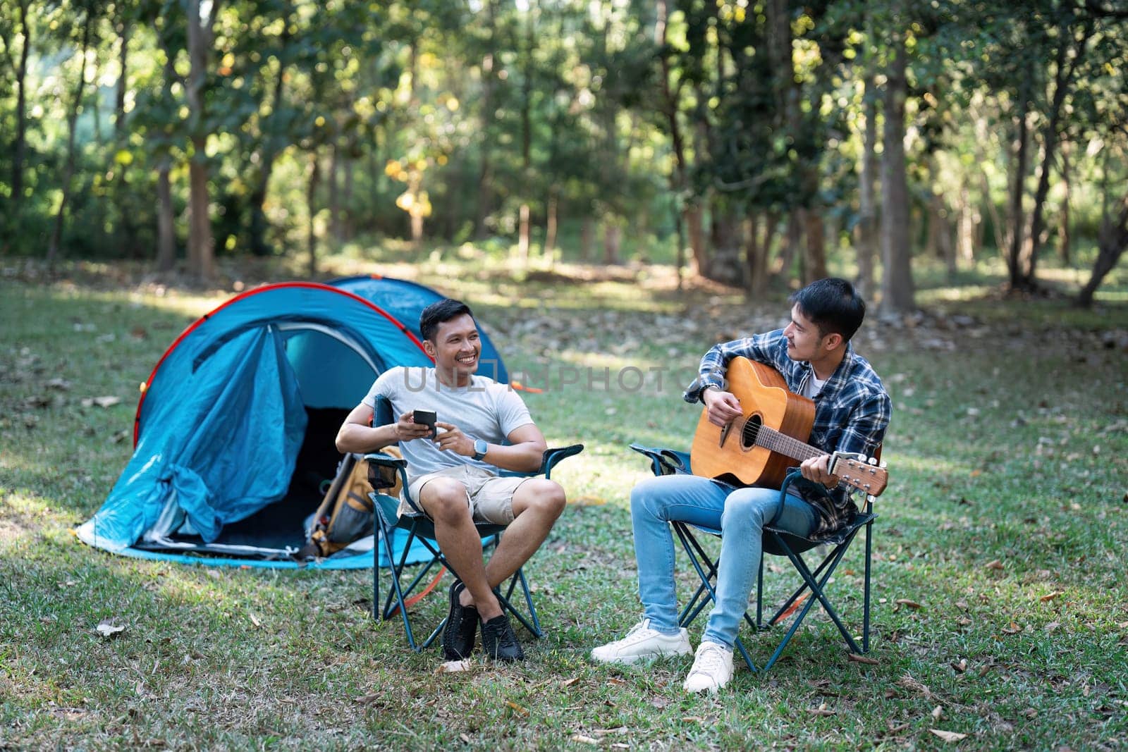 LGBTQIA Gay couple camping together in woods for holidays and relax on guitar together by itchaznong