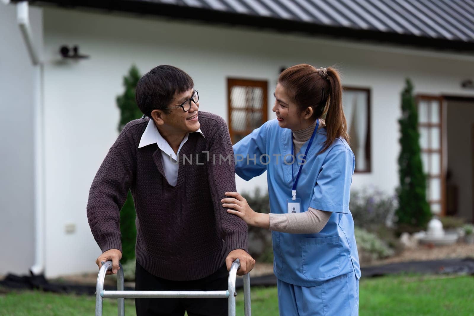 Nurse or caregiver helps elderly walk by using walker in garden by itchaznong