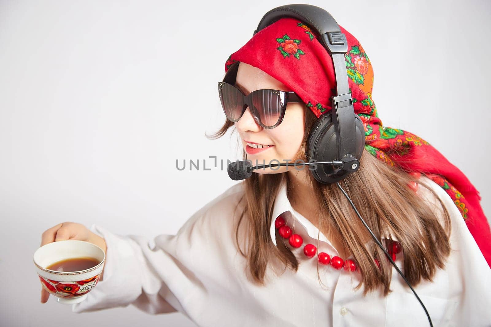 Portrait of young girl in a bright red scarf and large headphones with a microphone. A woman who is radio or television presenter with cap of tee. Funny female telecom operator. Freelancer at work