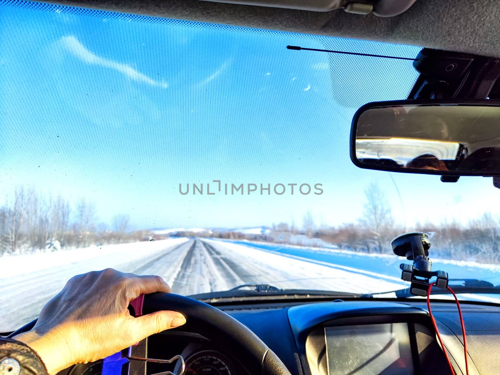 Hand of woman on the steering wheel in car and view through the windshield of a winter road with snow-covered trees