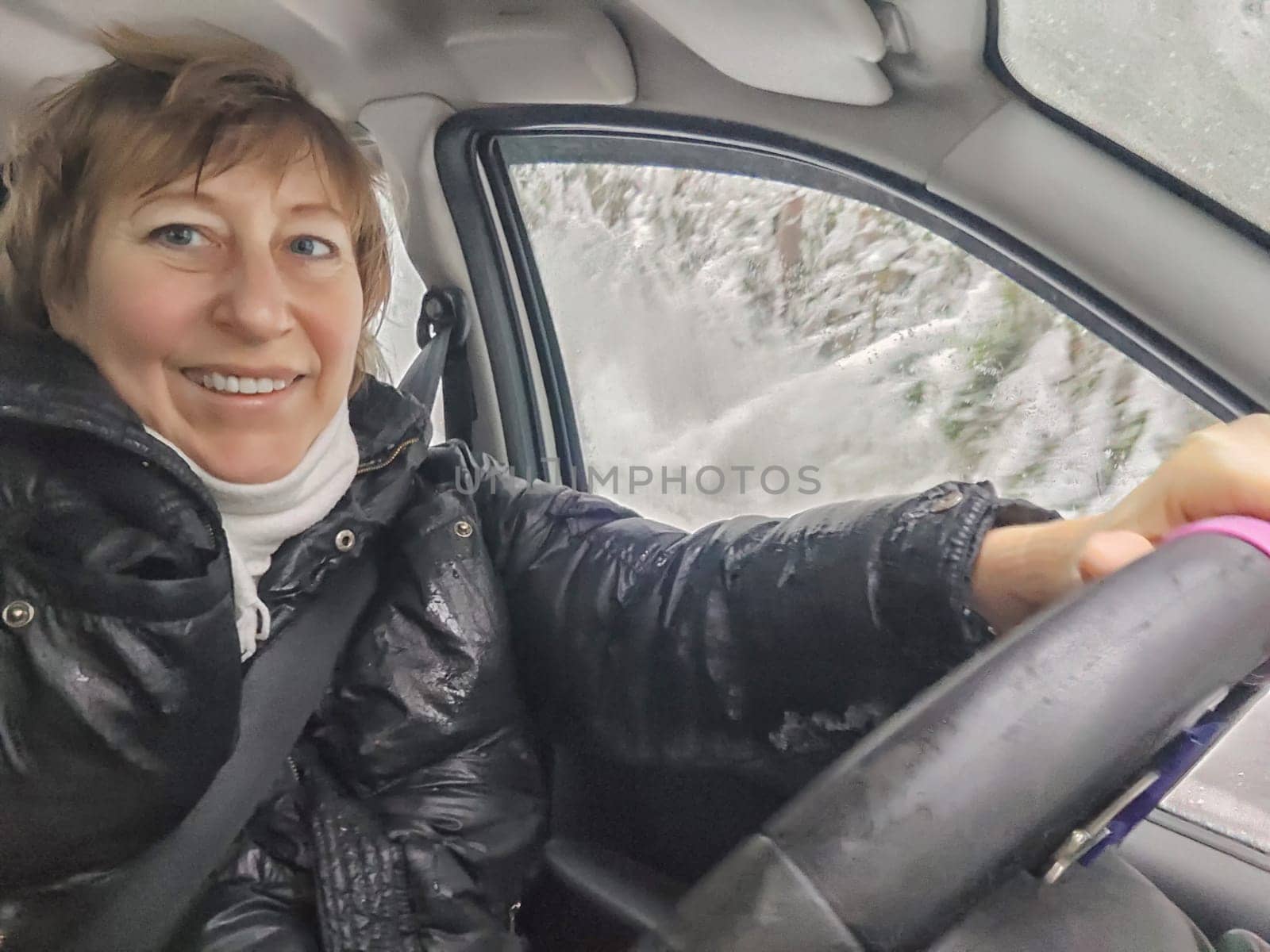 Funny shaggy-haired girl or a middle-aged woman drives a car in winter, autumn, and spring in the cold. A female driver on a solo trip