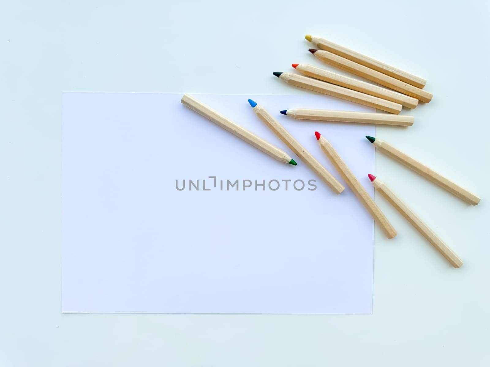 Colored pencils on table, on paper, on white background. Top view. High quality photo
