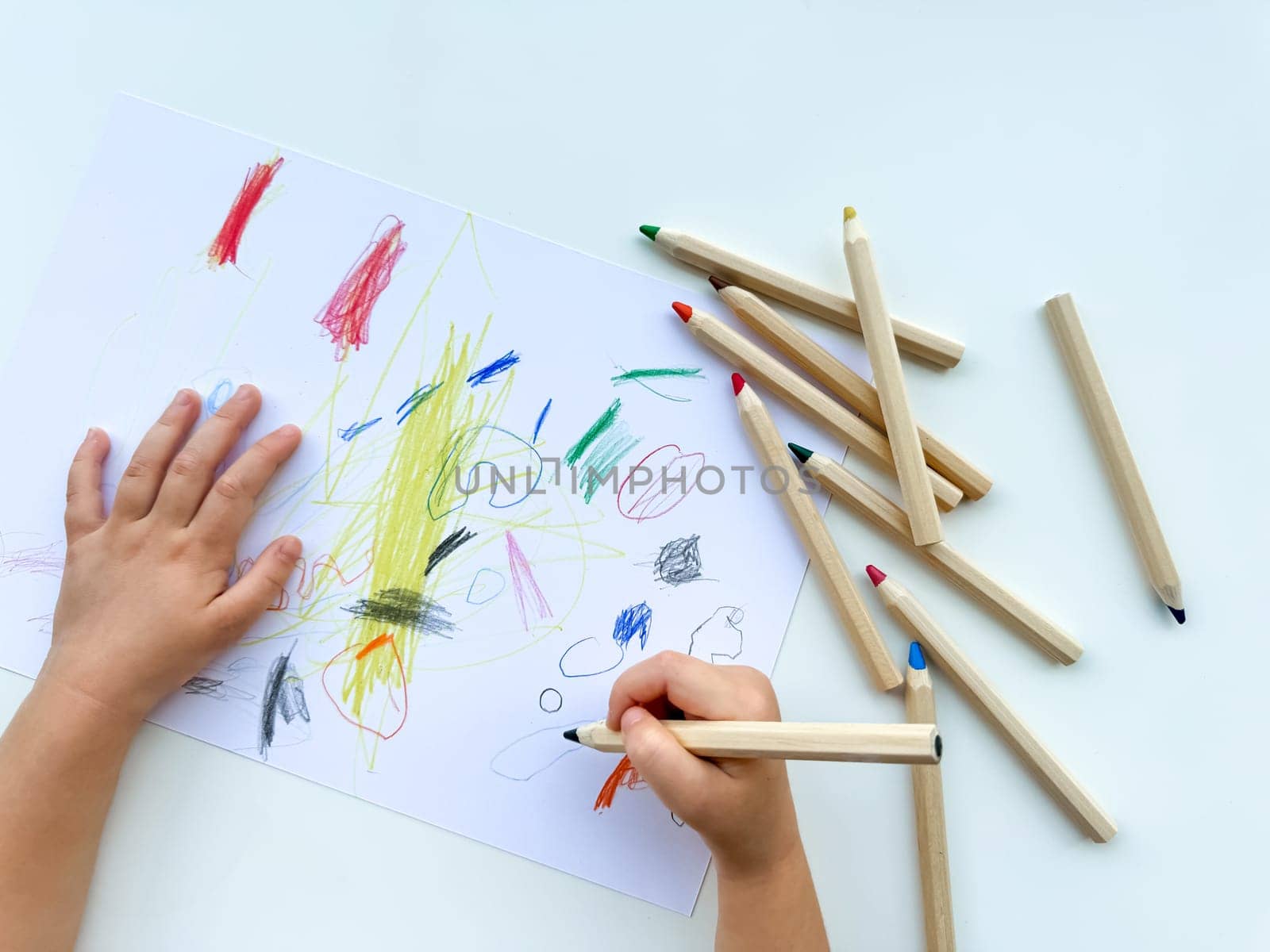 small child draws with colored pencils on paper on white table. High quality photo