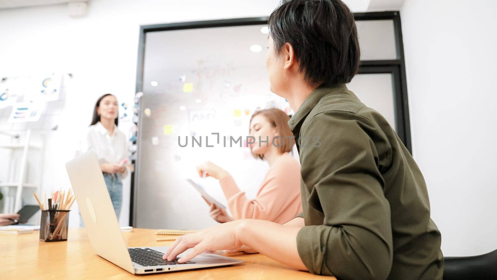 Young beautiful investor shares marketing strategy with attentive businesswoman in front of a glass board with colorful sticky notes and mind maps at creative business meeting room. Immaculate.