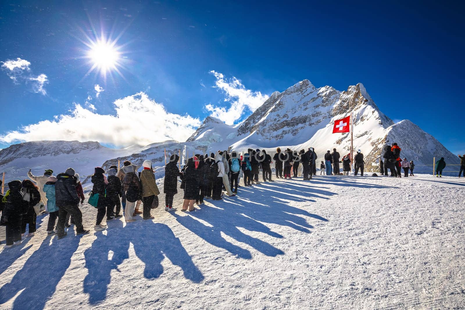 Tourists waiting in line to take a photo in front of Swiss flag on Jungfraujoch peak by xbrchx