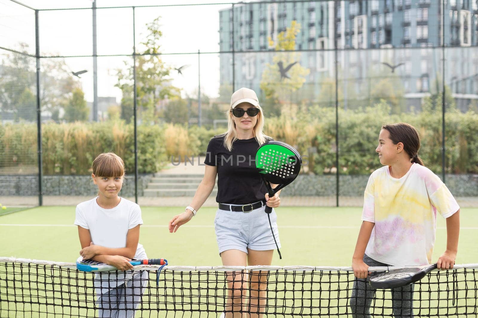 Young sporty woman with children playing padel game in court on sunny day. High quality photo