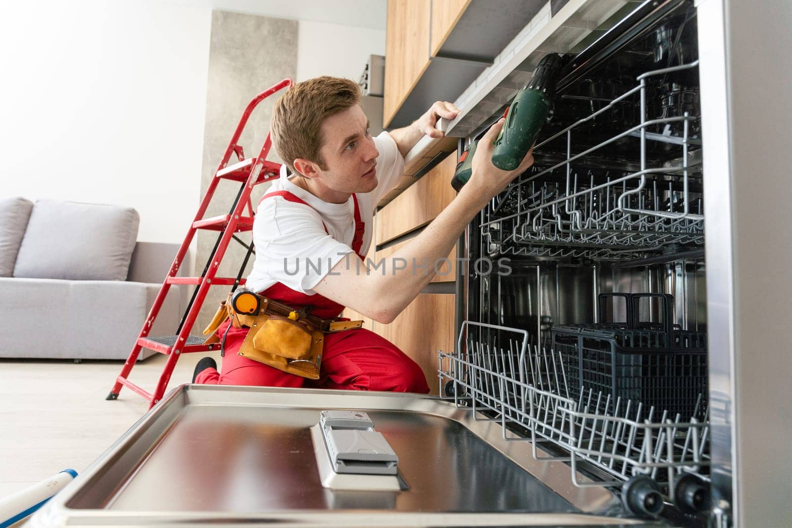 Repairman checks operating state of dishwasher in kitchen.