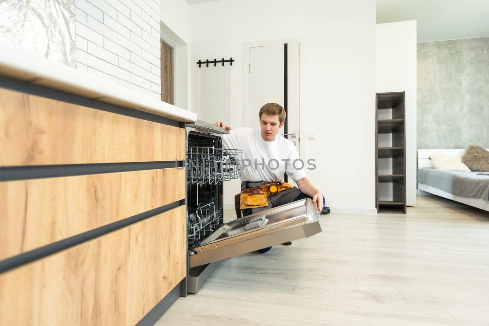 Repairman checks operating state of dishwasher in kitchen.