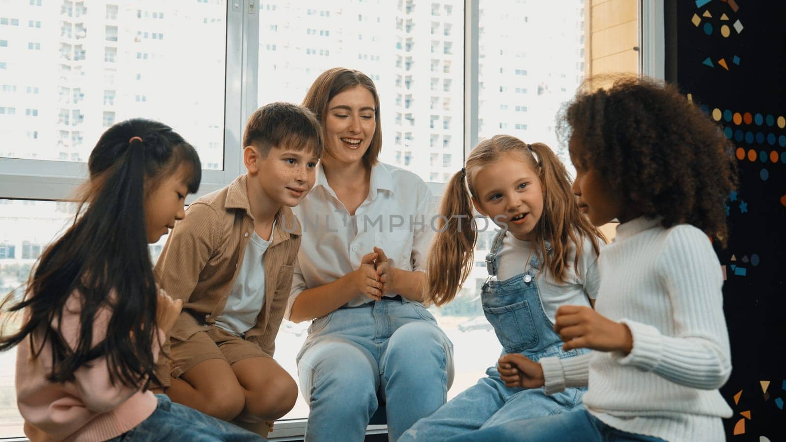 Smart caucasian teacher teaching while sitting on floor together surrounded by diverse students. Professional instructor playing with multicultural learner. Creative education concept. Erudition.