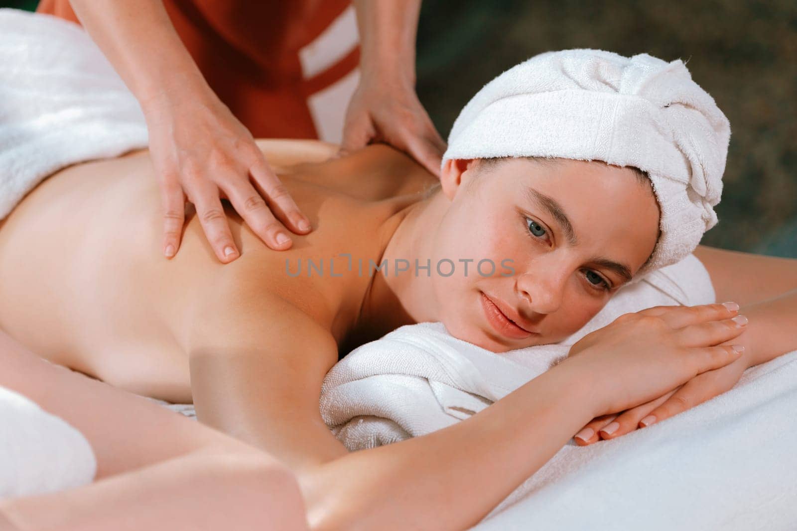 Beautiful young woman received a back massage on a spa bed from professional masseuse. Attractive female relaxes deeply by skilled hands of the massage therapist. Surrounded with nature. Tranquility.
