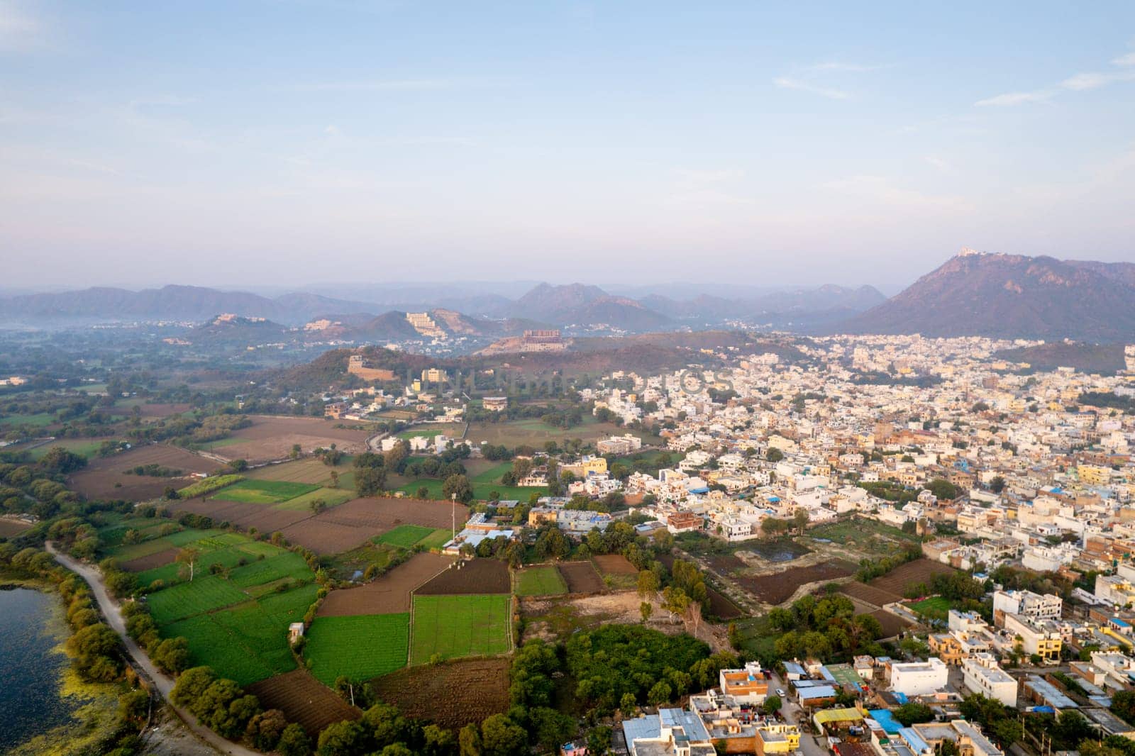 Aerial drone shot over udiapur, jaipur, kota,, cityscape with homes, houses, buildings and aravalli hills and lakes before sunrise and fog in distance by Shalinimathur