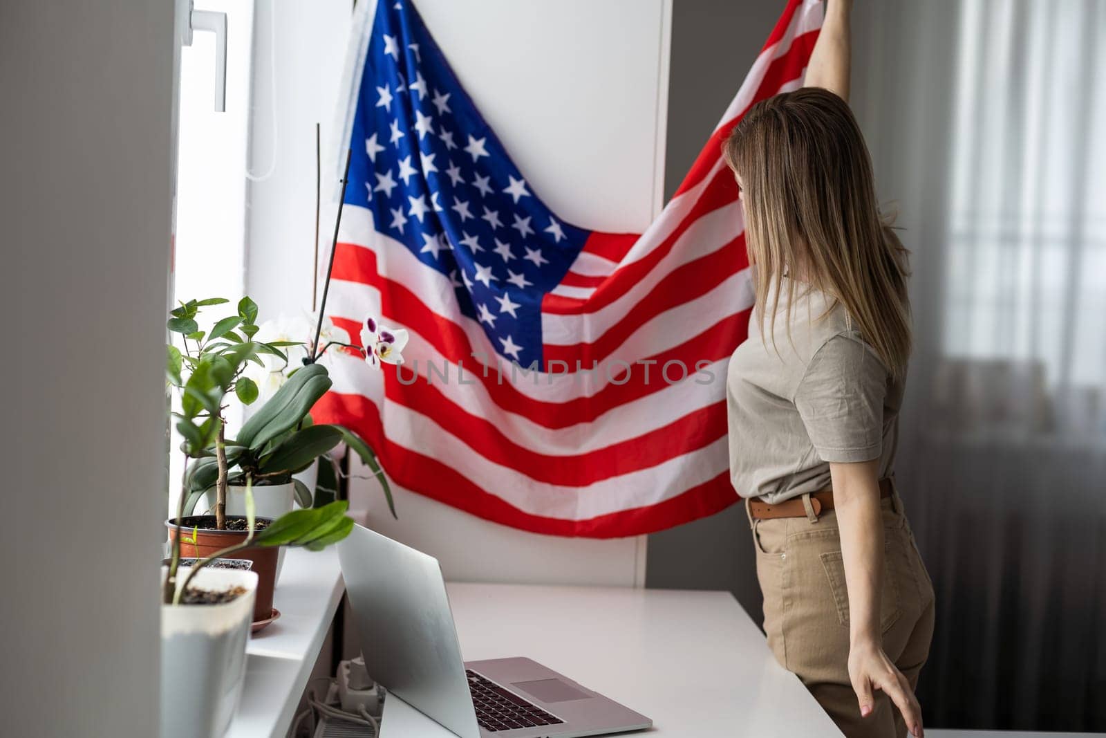 Happy woman employee sitting wrapped in USA flag, shouting for joy in office workplace, celebrating labor day or US Independence day. High quality photo