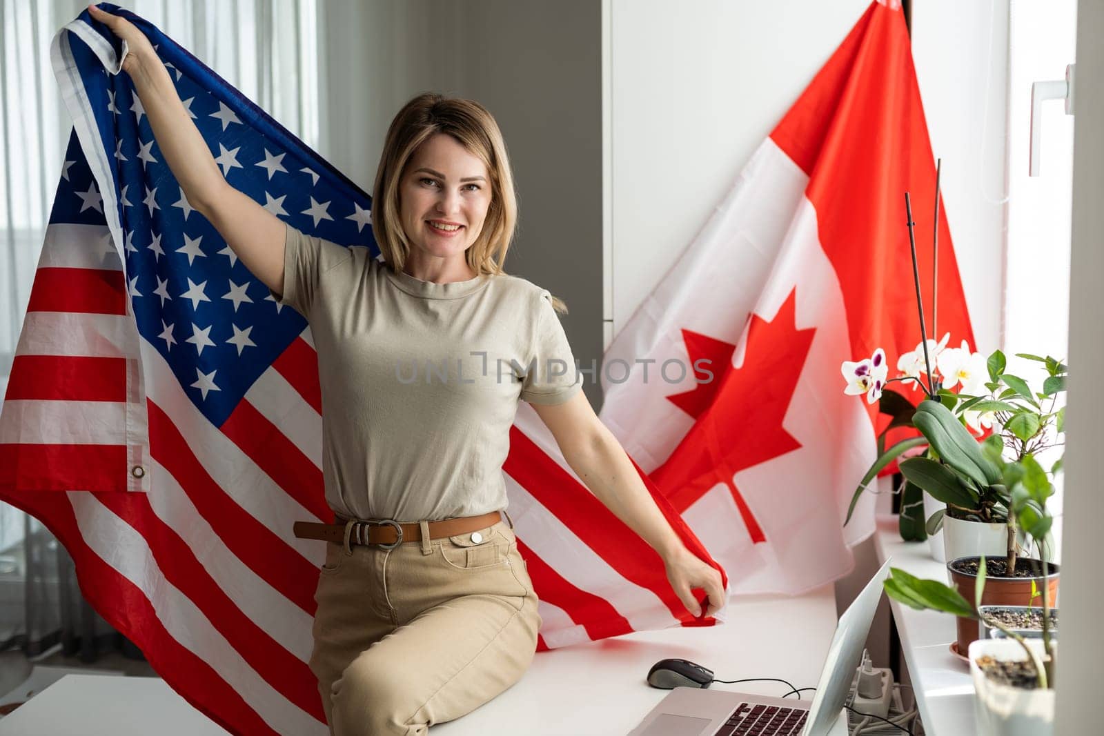Portrait of happy young woman with USA flag learning American English online from home using laptop. Smiling female student sitting at table and taking online educational course in foreign languages. High quality photo