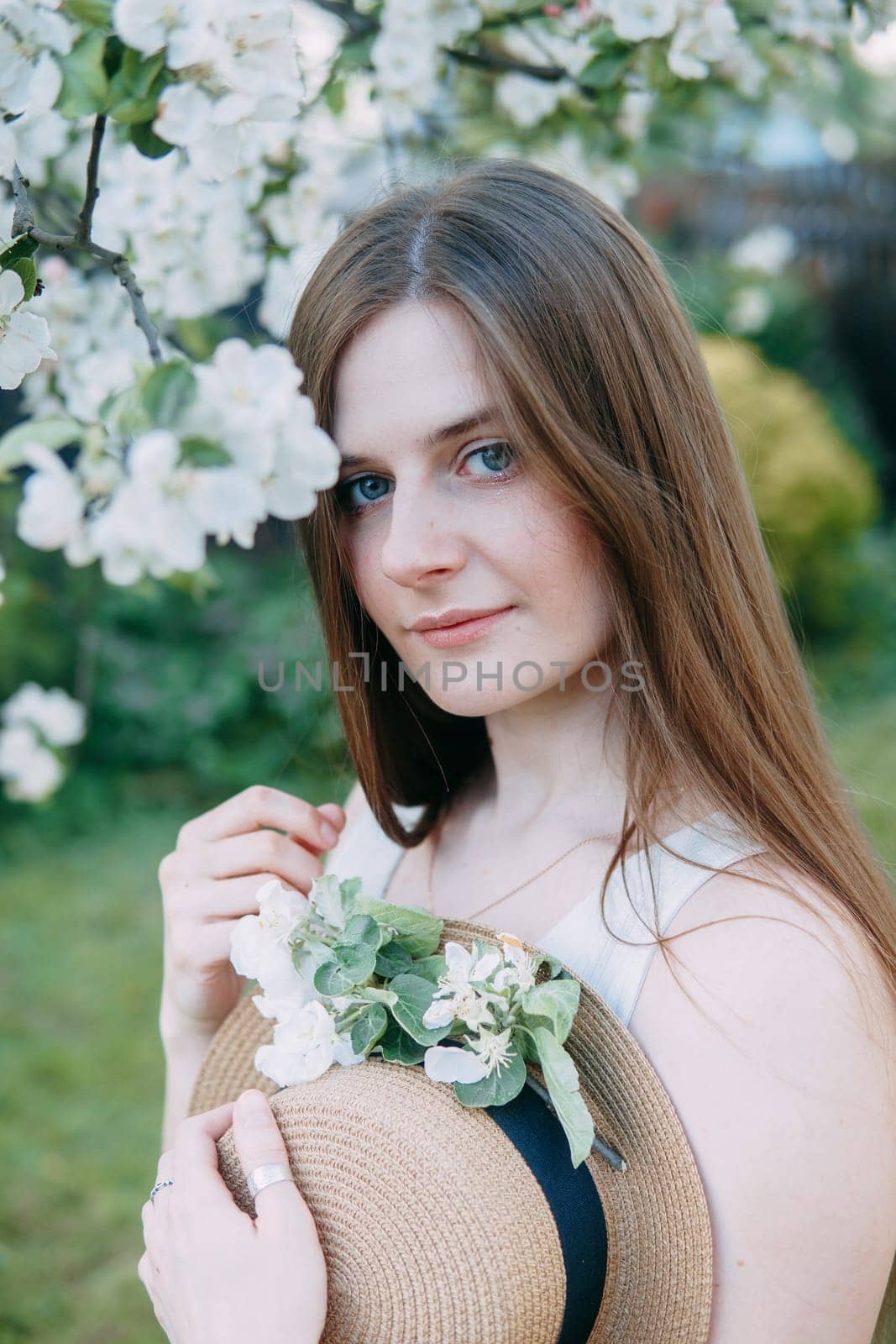 Beautiful young girl in white dress and hat in blooming Apple orchard. Blooming Apple trees with white flowers