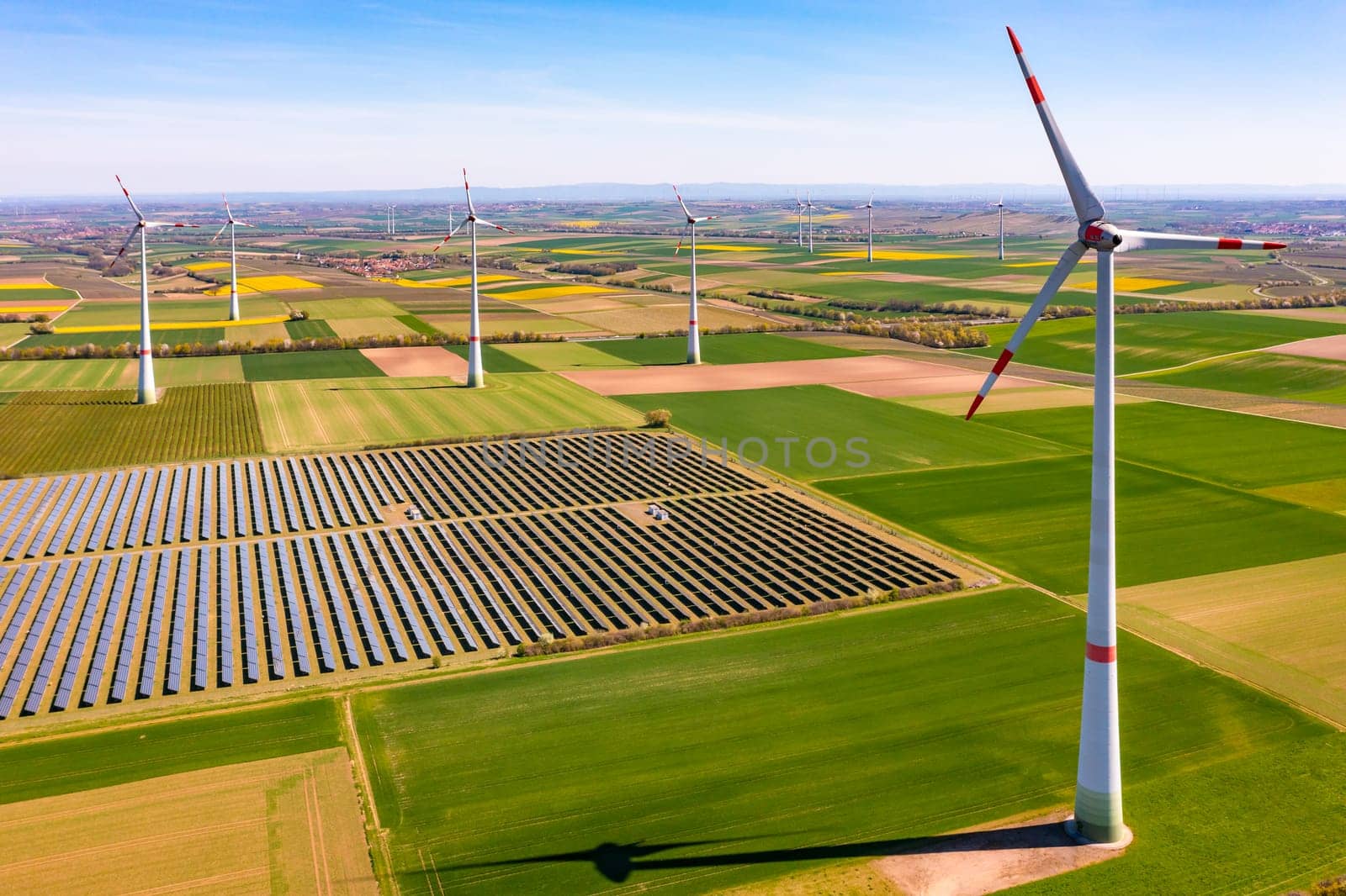 Aerial view of huge wind turbines between agricultural land and a solar park in rural area, Germany by astrosoft
