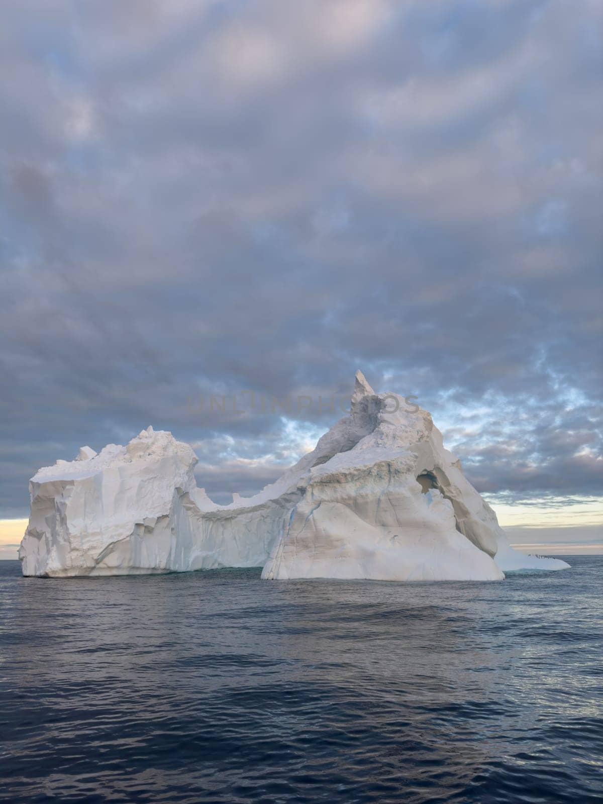 A huge high breakaway glacier drifts in the southern ocean off the coast of Antarctica at sunset, the Antarctic Peninsula, the Southern Arctic Circle, azure water, cloudy weather. High quality photo