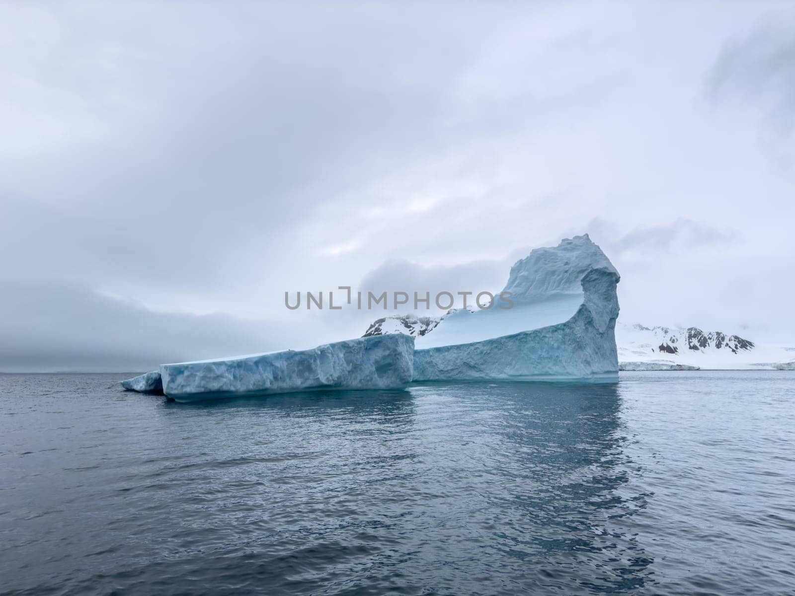 A huge high breakaway glacier drifts in the southern ocean off the coast of Antarctica at sunset, the Antarctic Peninsula, the Southern Arctic Circle, azure water, cloudy weather by vladimirdrozdin