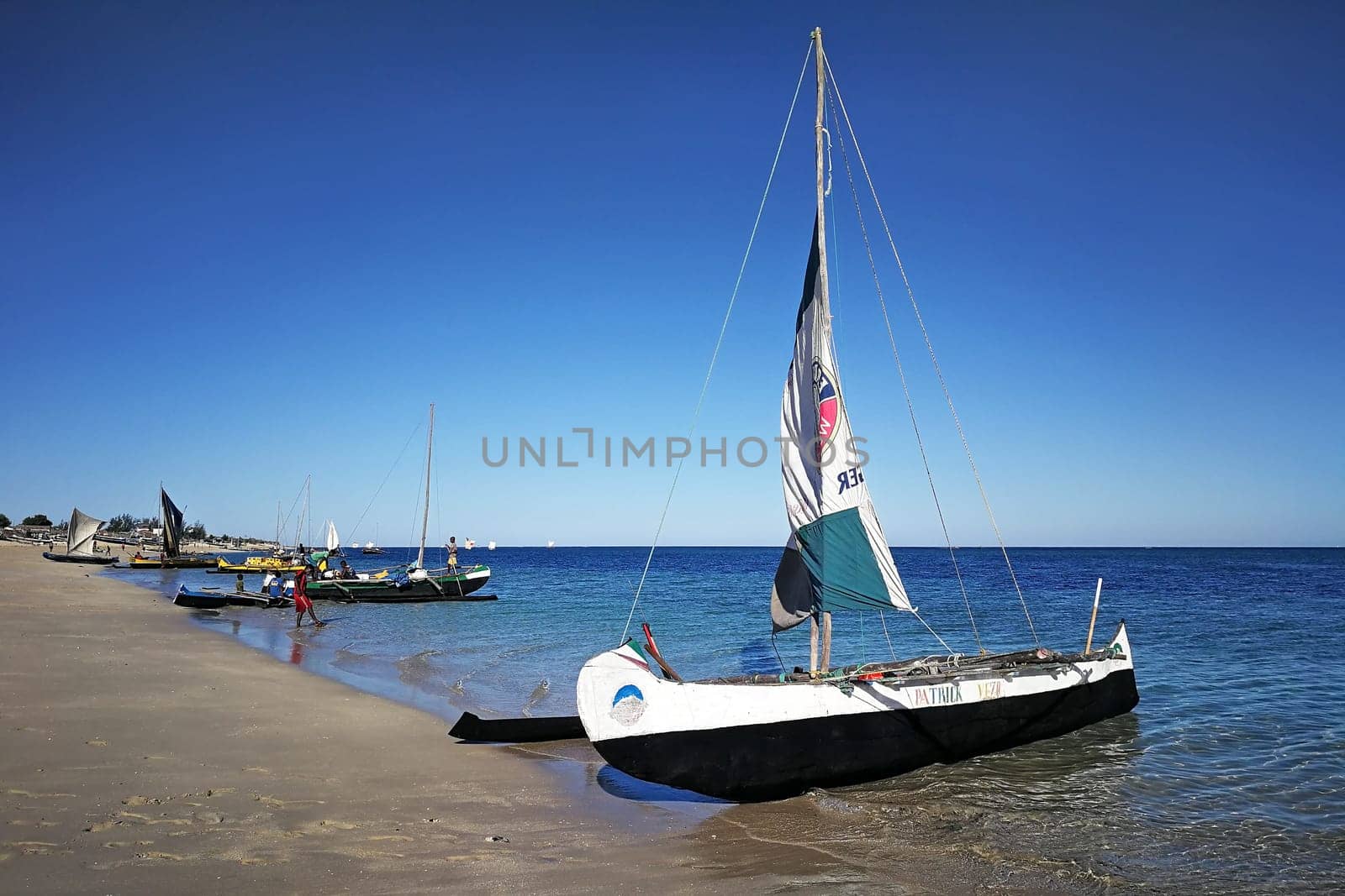 Anakao, Madagascar - May 03, 2019: Fisherman piroga (small fishing boat with sail) waiting at the coast on sunny day, more ships with Malagasy locals in background. Fish is one of main sources of food by Ivanko