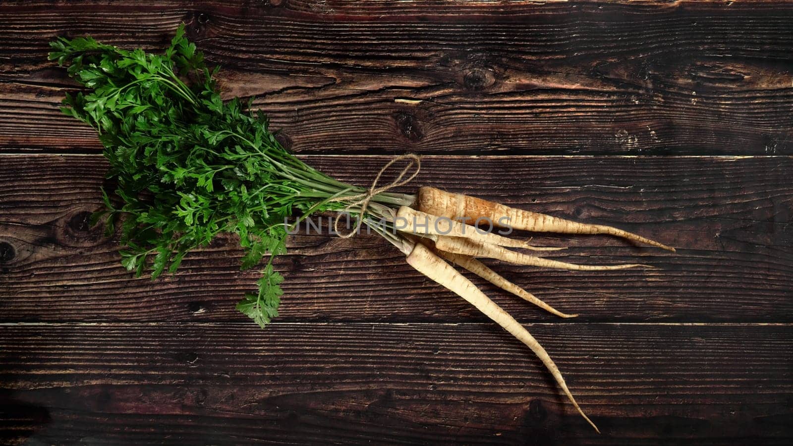 Bunch of parsnip roots with green leaves on rustic dark wooden board, view from above