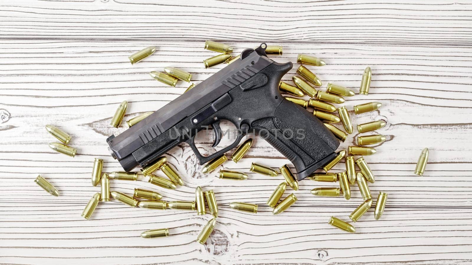 Top down view - modern black simple gun and yellow brass ammunition bullets scattered around on white wooden boards desk by Ivanko