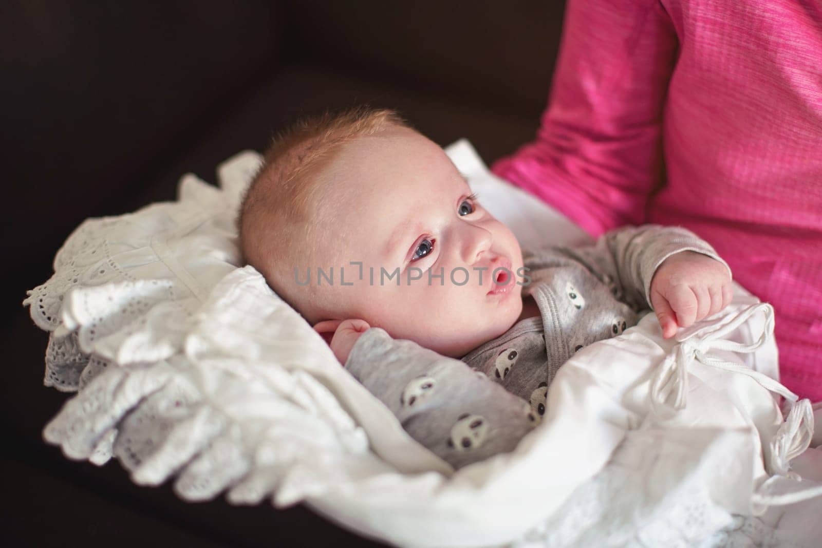 Mother hold infant baby boy on her hands, toddler covered in white blanket